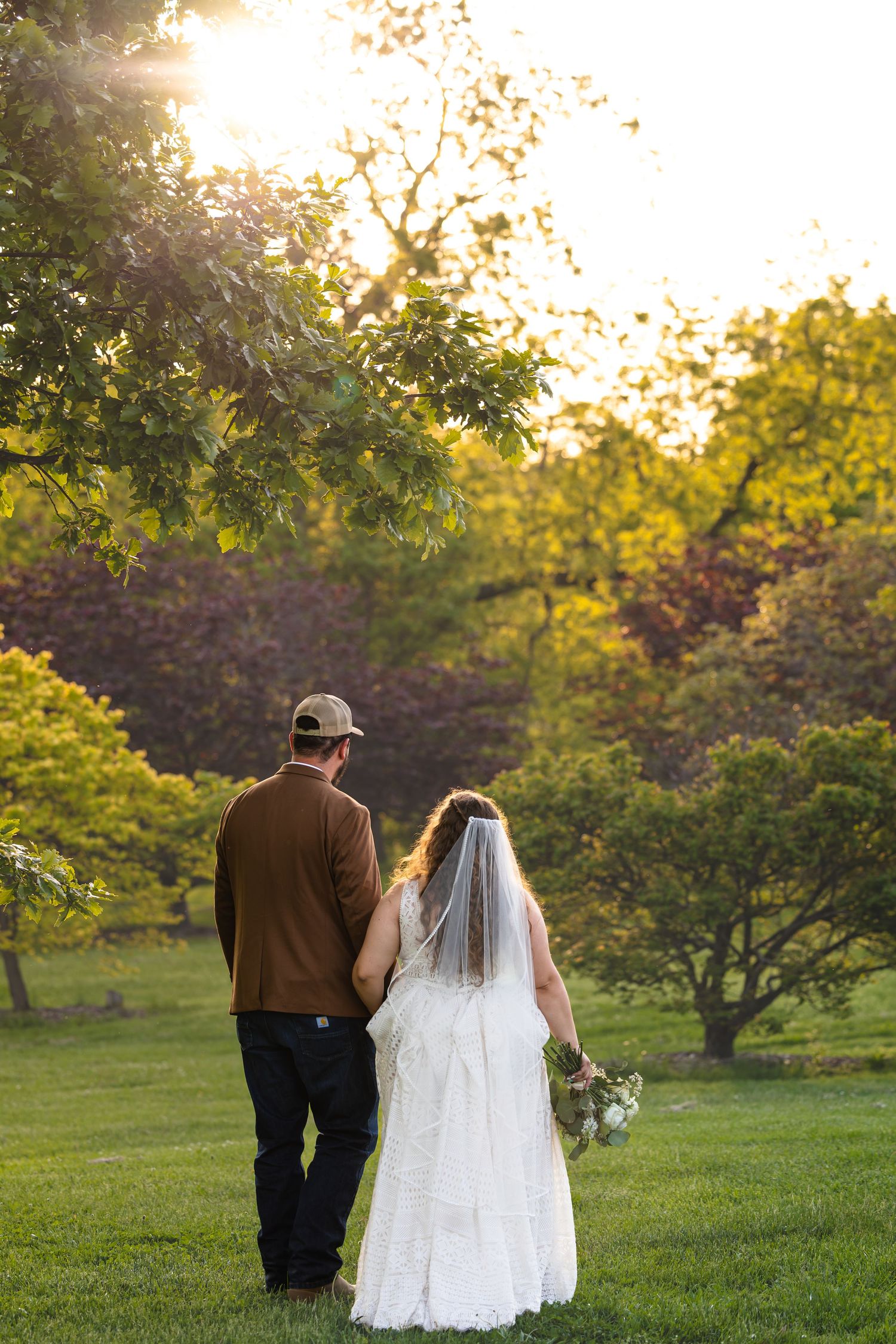 bride and groom holding hands walking away from the camera toward trees on wedding day during sunset portraits in Columbia Missouri