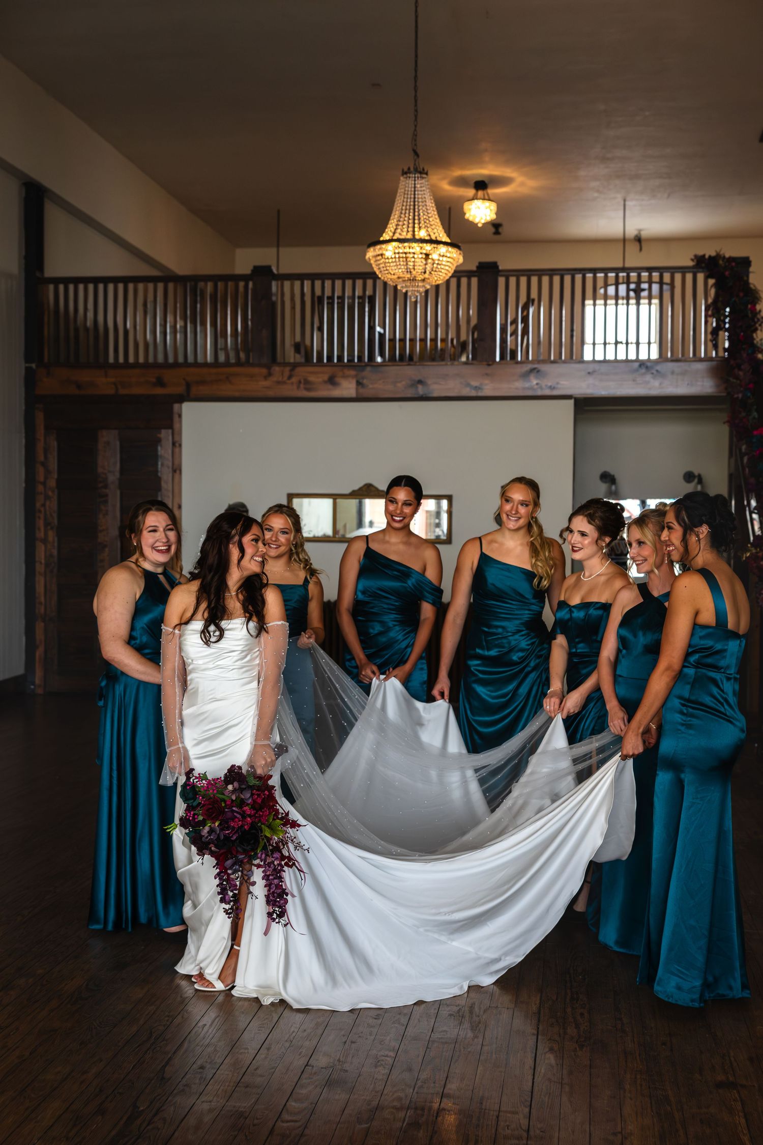 bridal party holding bride's dress and veil smiling at each other during wedding party photos on wedding day near Moberly and Columbia MO