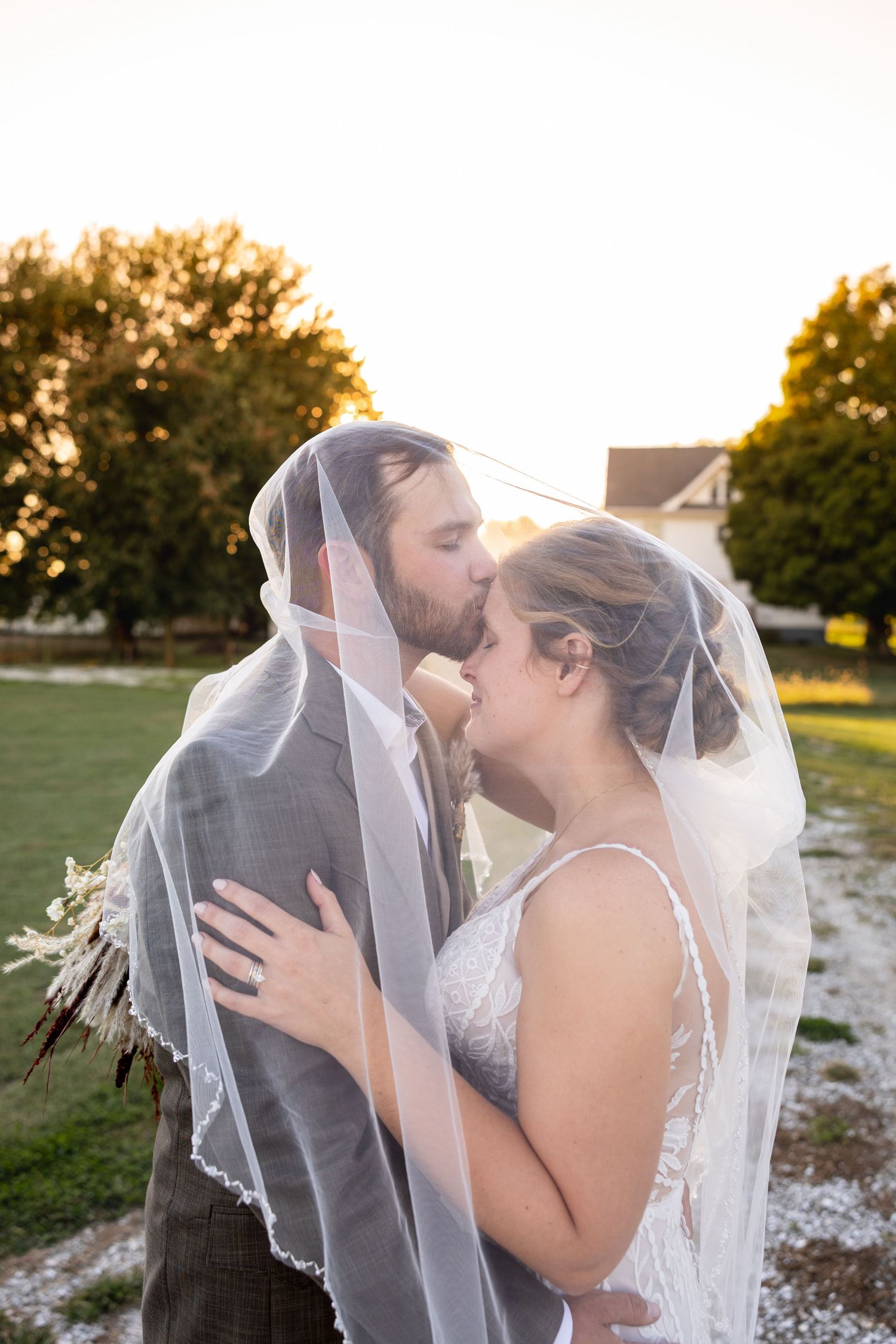 groom kissing bride's forehead during sunset wedding photos on wedding day in Moberly MO