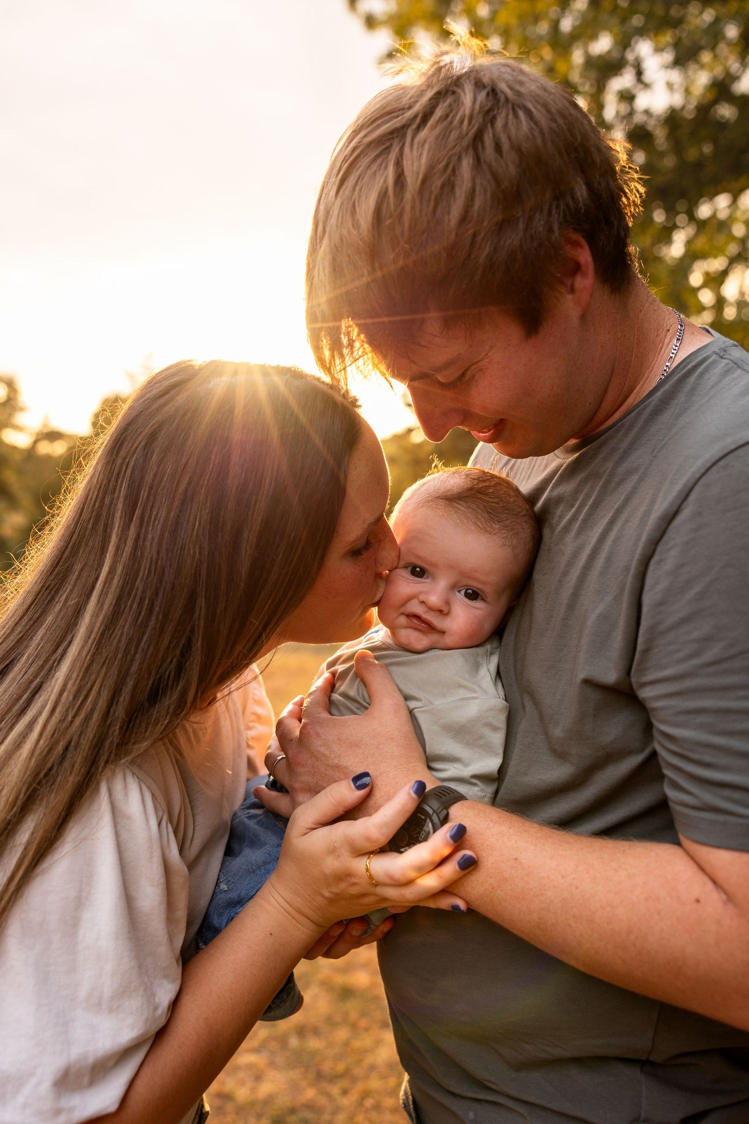 mom kissing baby's face while dad holds baby for sunset family photos in fields near Columbia MO