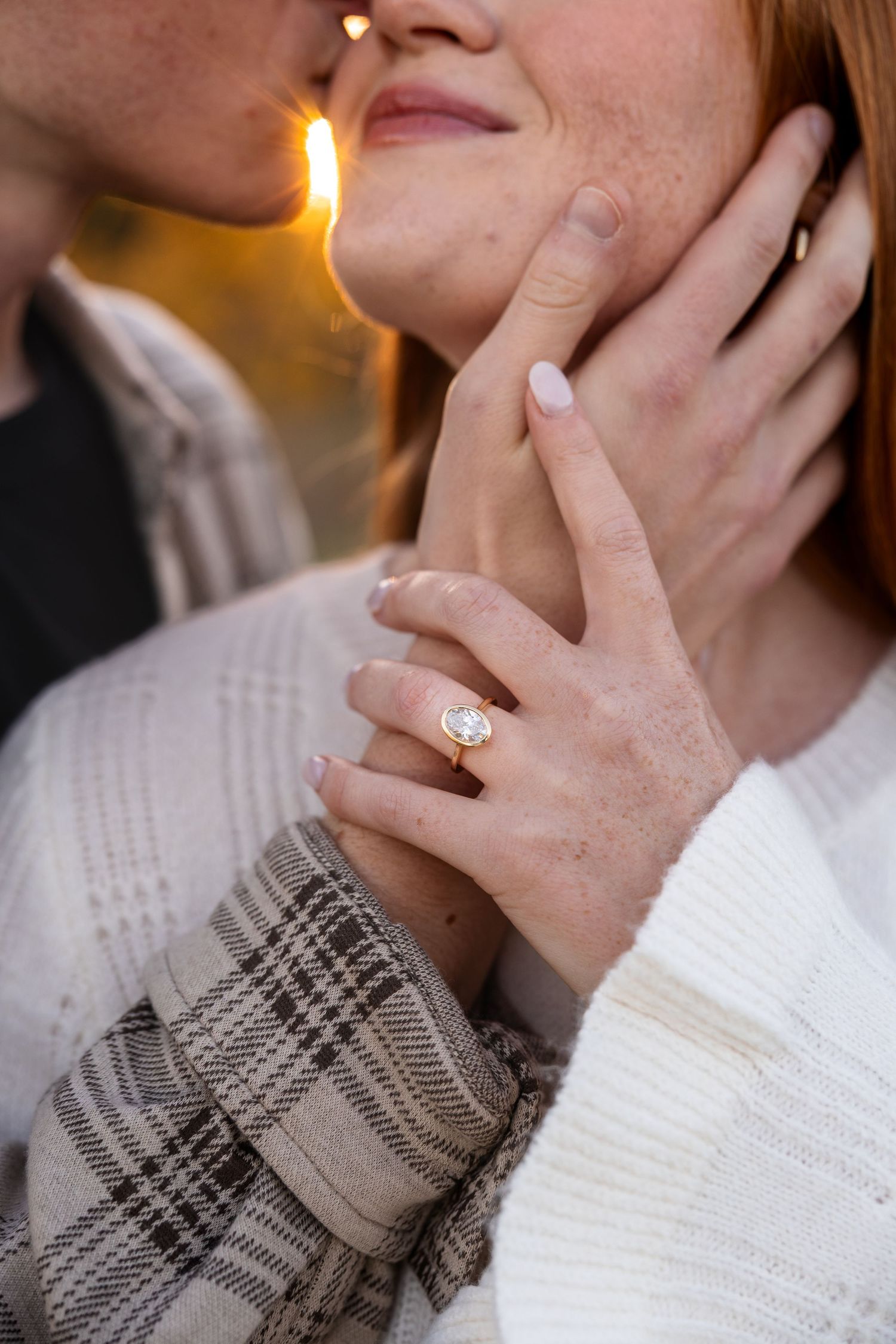 man holding woman's face and kissing her cheek with woman's engagement ring hand highlighted in this photo for engagement photos
