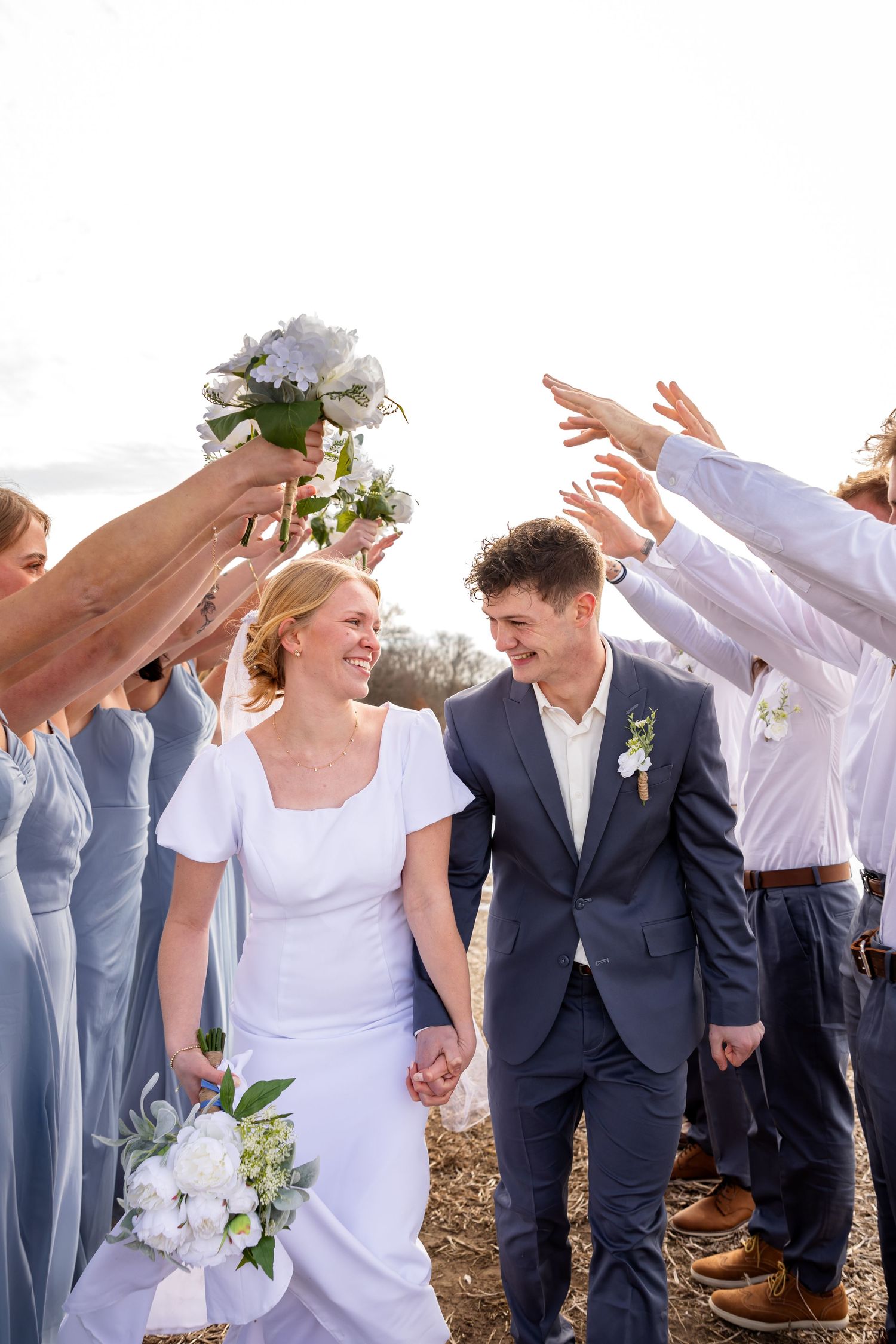 bride and groom holding hands smiling at each other while walking with bridal party on wedding day in northern Missouri