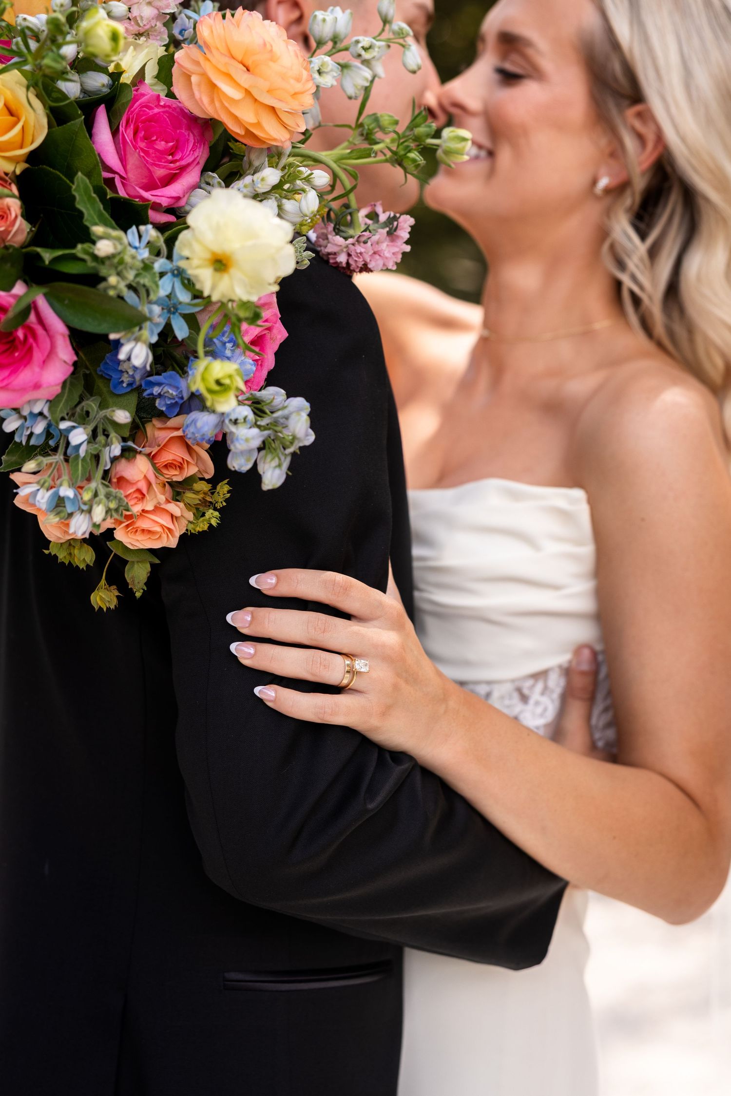 bride holding groom's arm with bouquet wrapped around his neck smiling at each other highlighting brides ring in STL MO