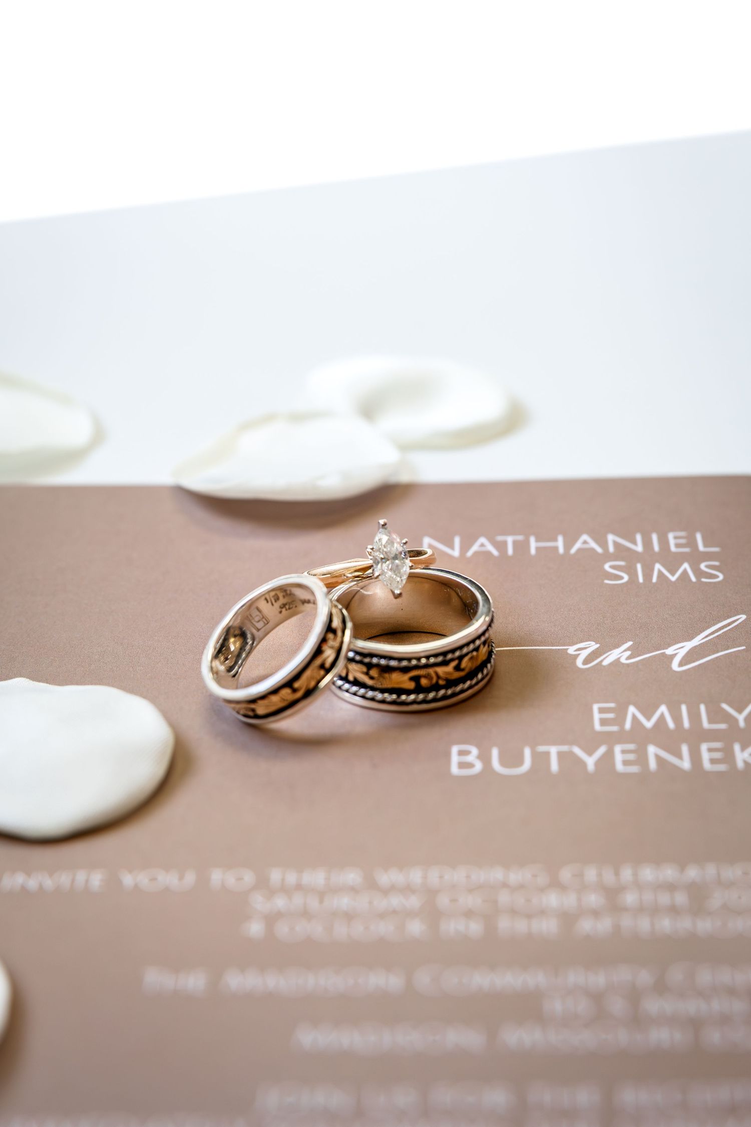bride and groom wedding rings on their wedding invitation with flower petals for Wedding Detail Photos in Mid Missouri Wedding
