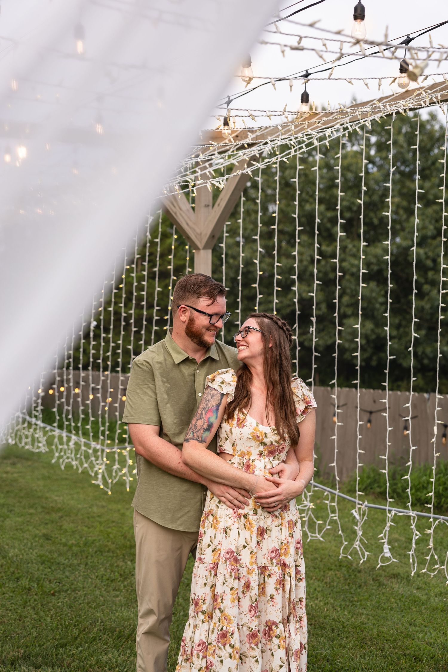 man and woman holding each other in embrace and smiling at each other under warm lights at wedding venue for engagement photos in mid MO