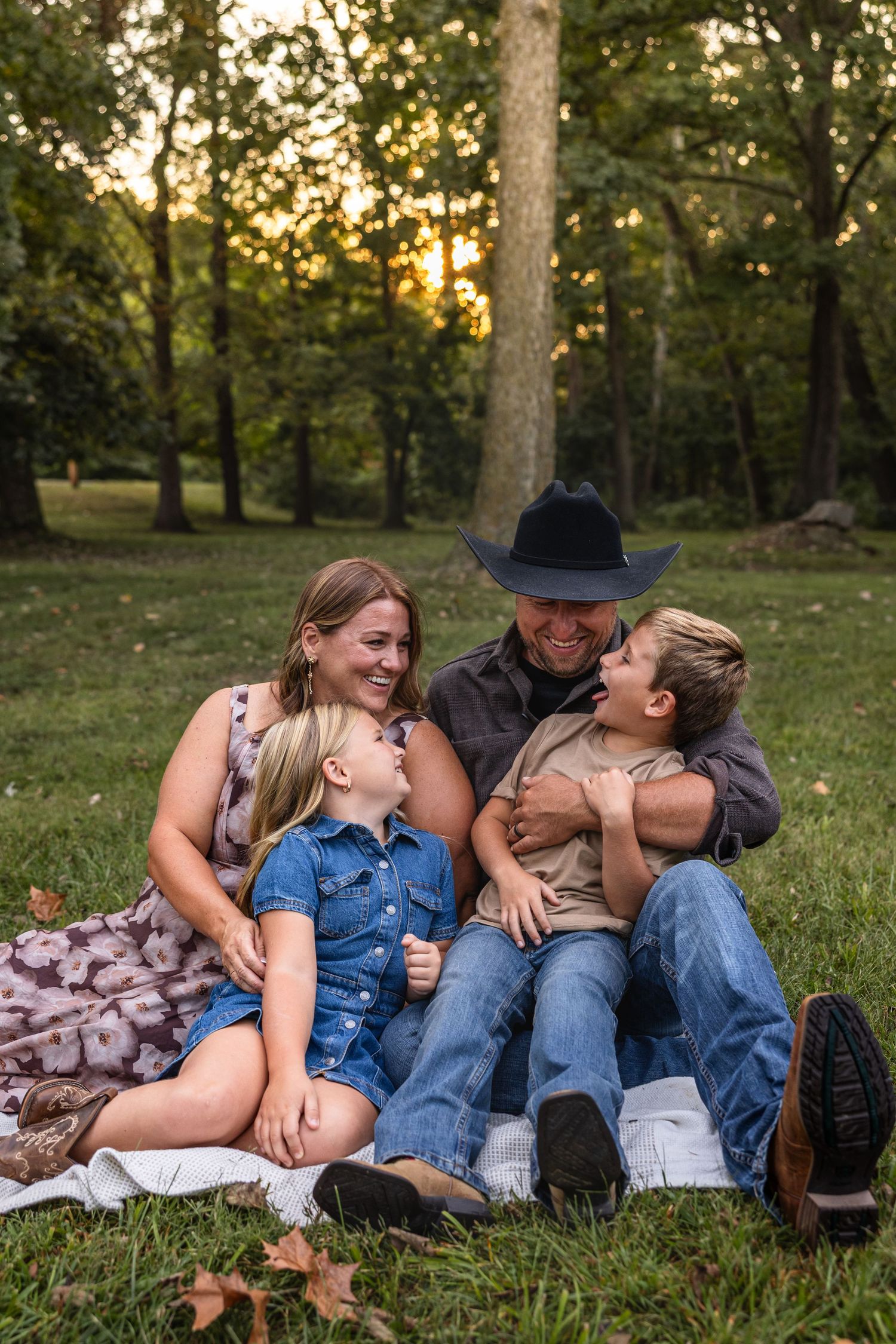 mom and dad sitting on ground in park with younger children sitting in their laps looking at each other for family photos in Mid Missouri