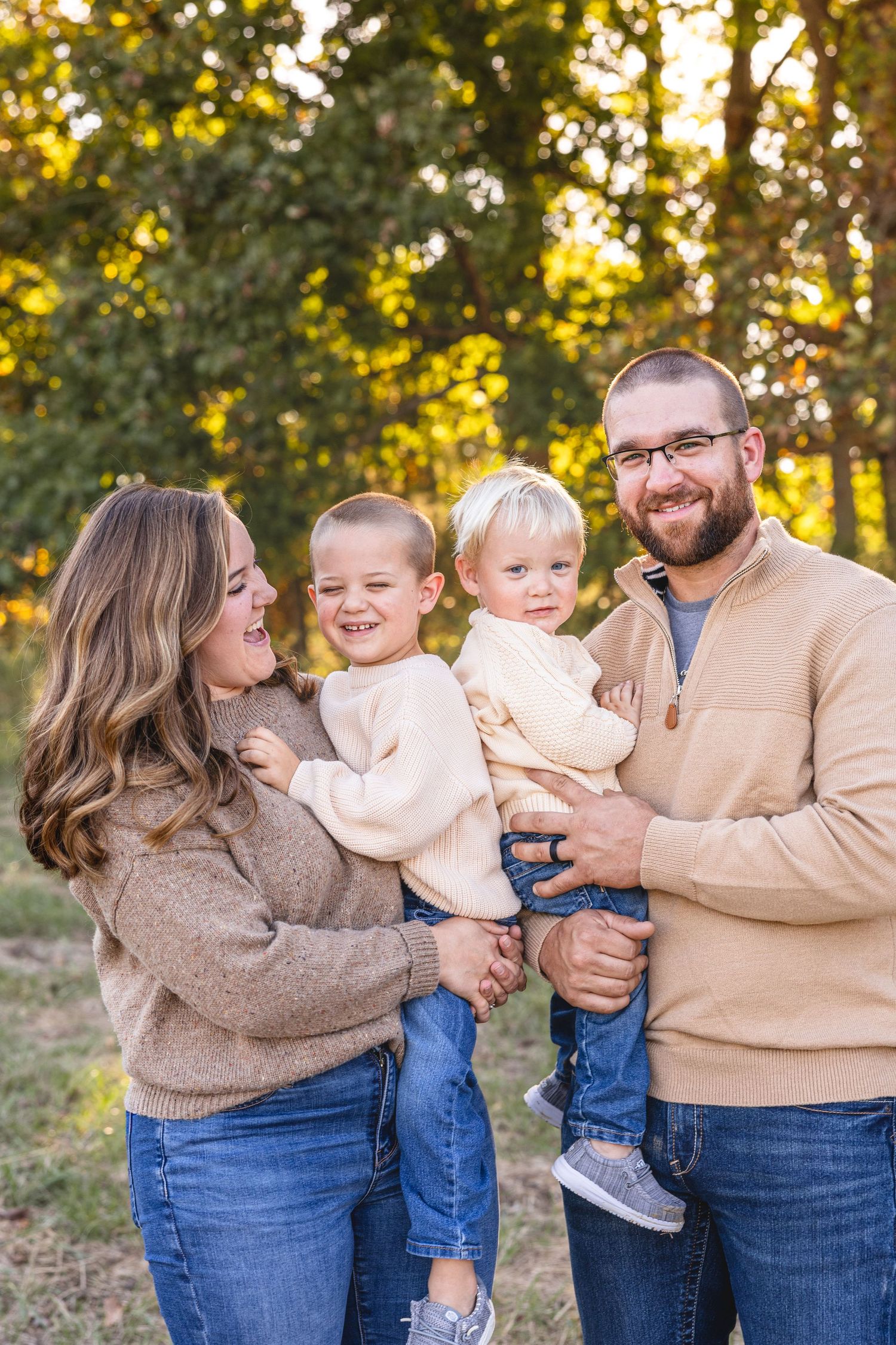 mom and dad holding toddler boys smiling at each other for fall family photos near Moberly MO