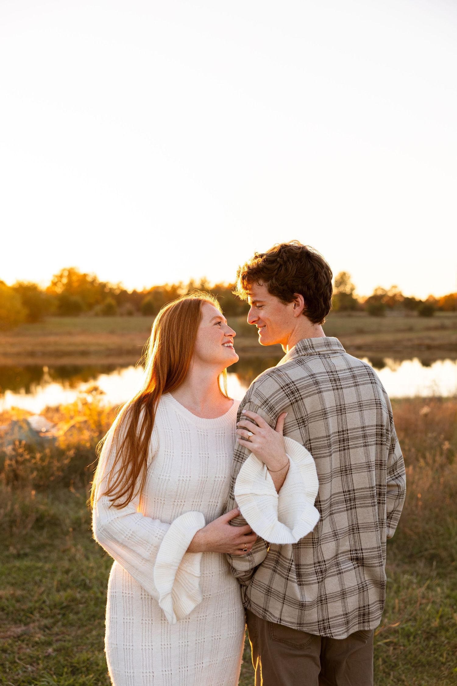 girl holding guys arm highlighting engagement ring in front of lake during sunset engagement photos in Mid Missouri near Columbia Missouri