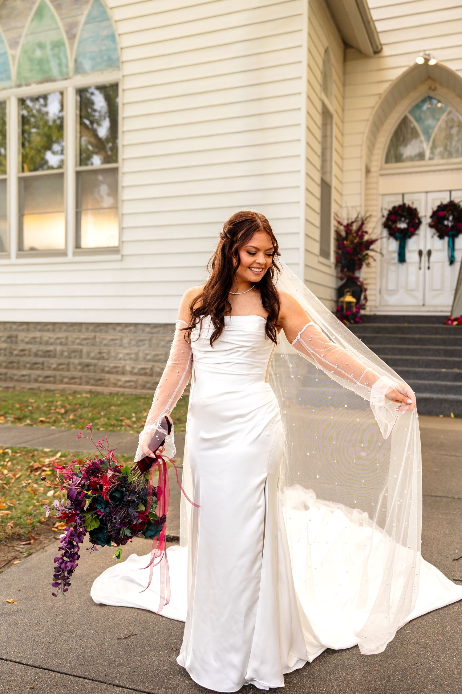 bride holding veil and bouquet in front of wedding chapel for wedding photos on wedding day near Columbia MO
