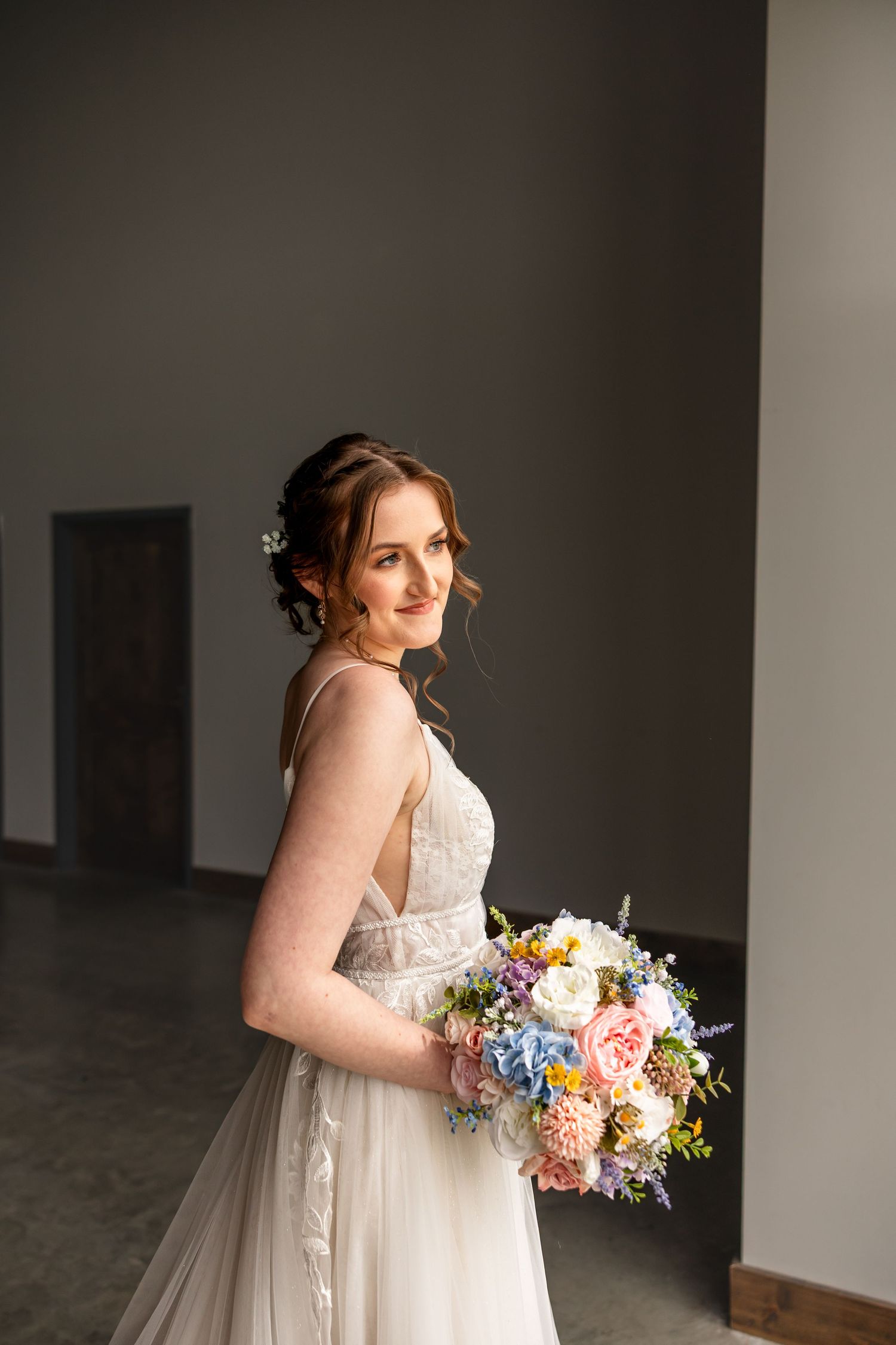 bride in wedding dress holding bouquet looking out the window and smiling for bridal photos on wedding day in Jefferson City MO