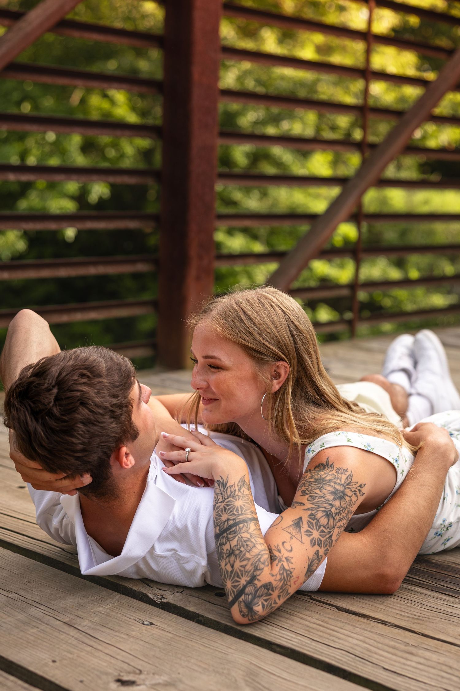 woman resting hands on top of man while laying on the ground smiling at each other for engagement photos on bridge in Columbia, Missouri