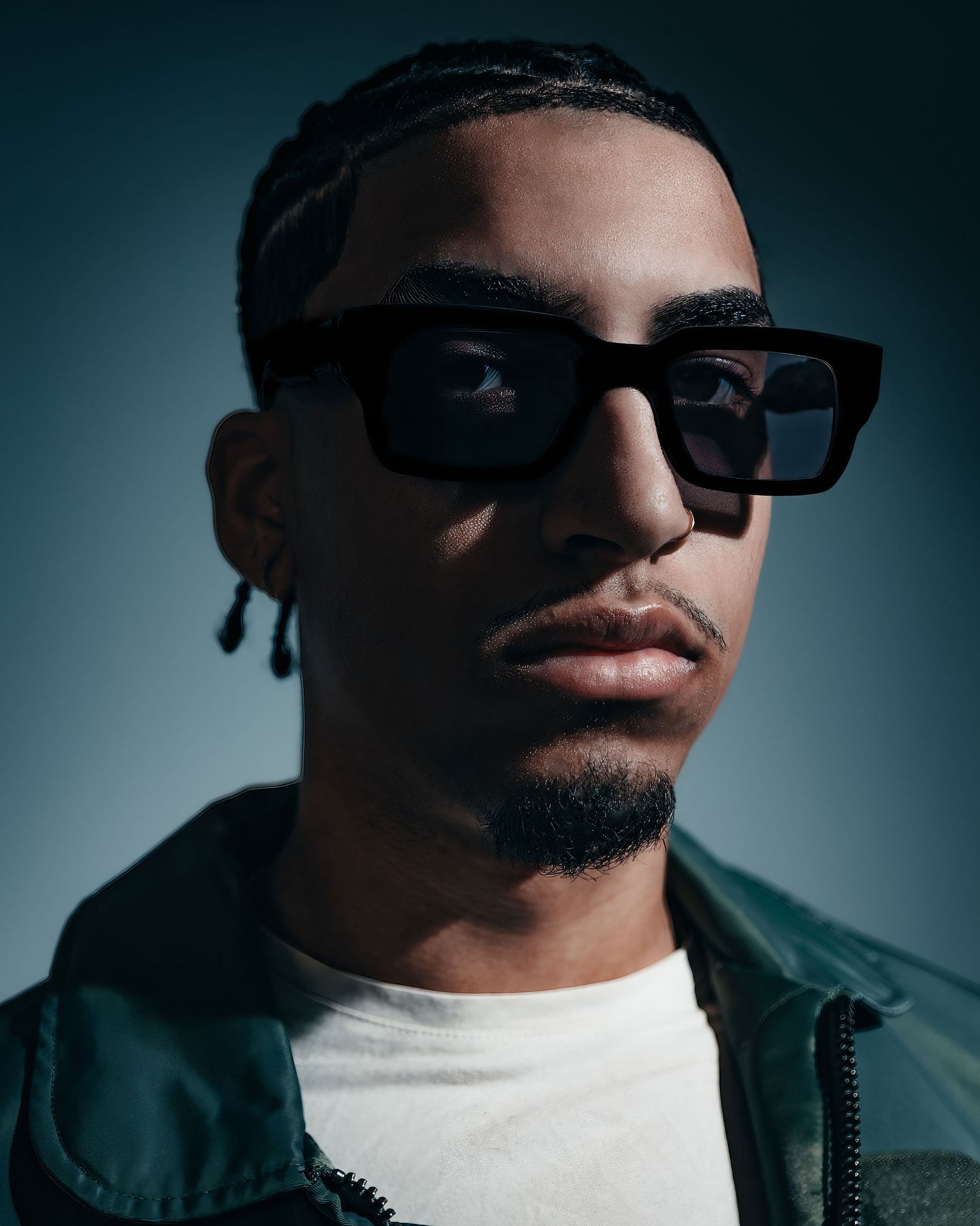 Dramatic close-up portrait shots in moody lighting showing sunglasses and white t-shirt.