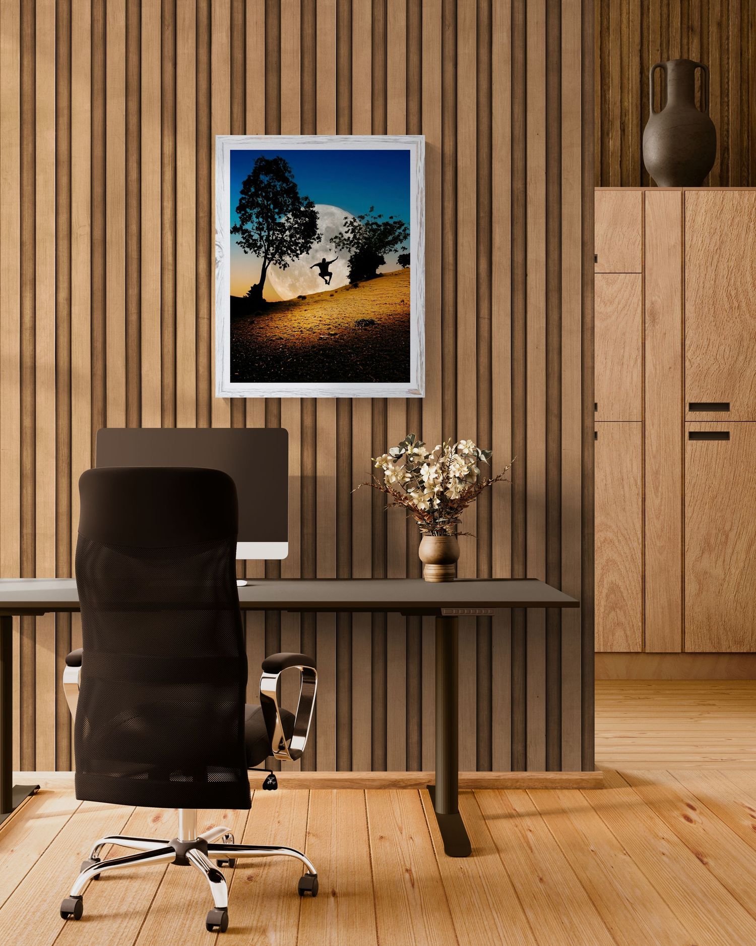 Modern home office with wood slat walls, black desk, ergonomic chair, and framed landscape artwork above a vase of dried flowers.