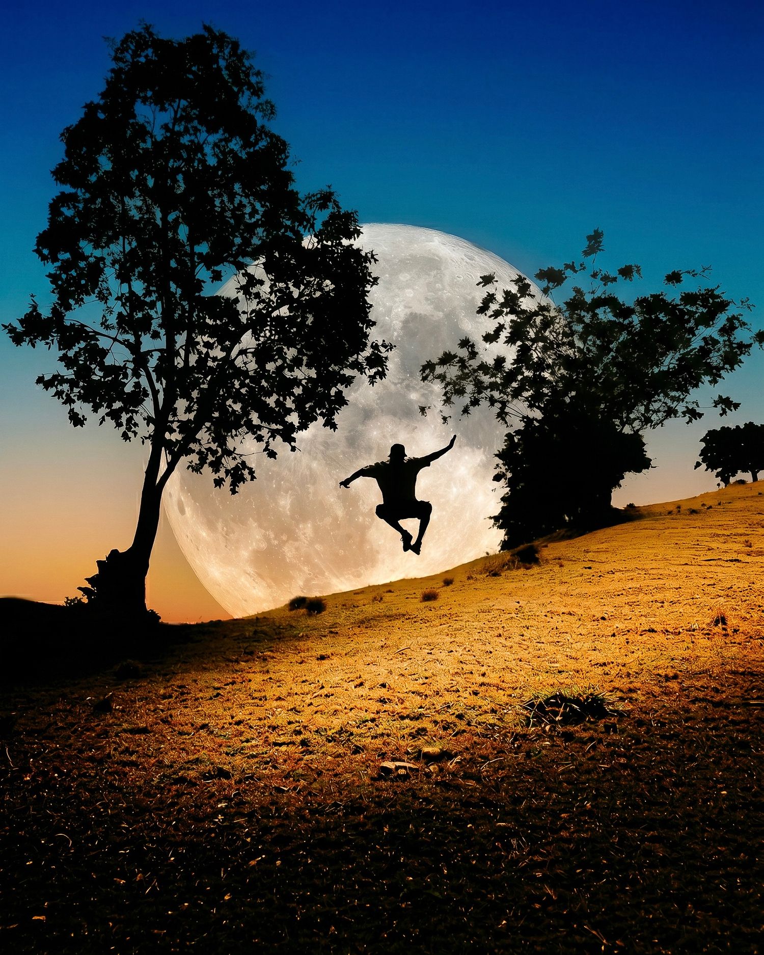 Silhouette of a person jumping against a giant full moon between two trees on a golden hillside at dusk.