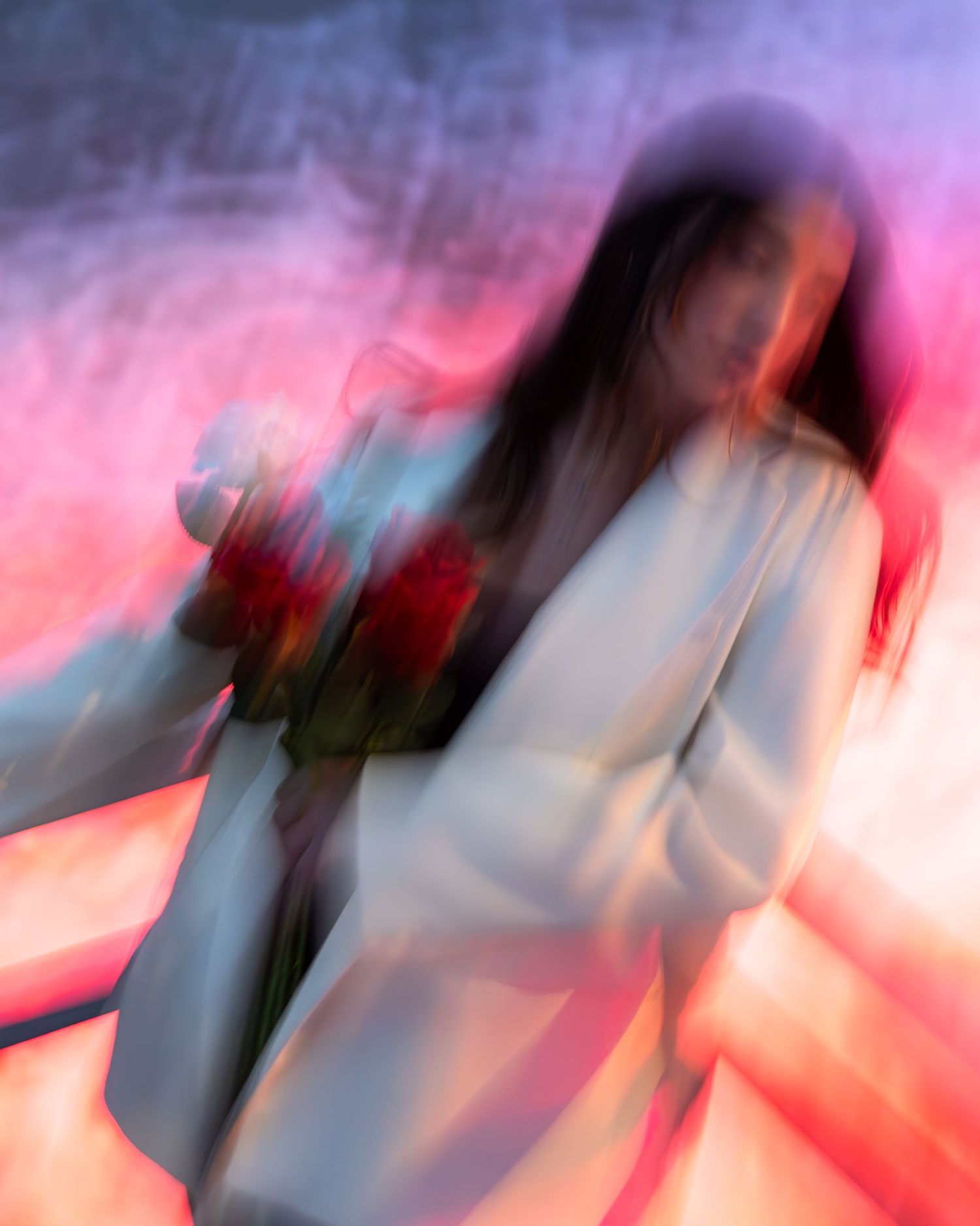 A woman in a white blazer holds red roses, bathed in dreamy pink and purple light with artistic motion blur.