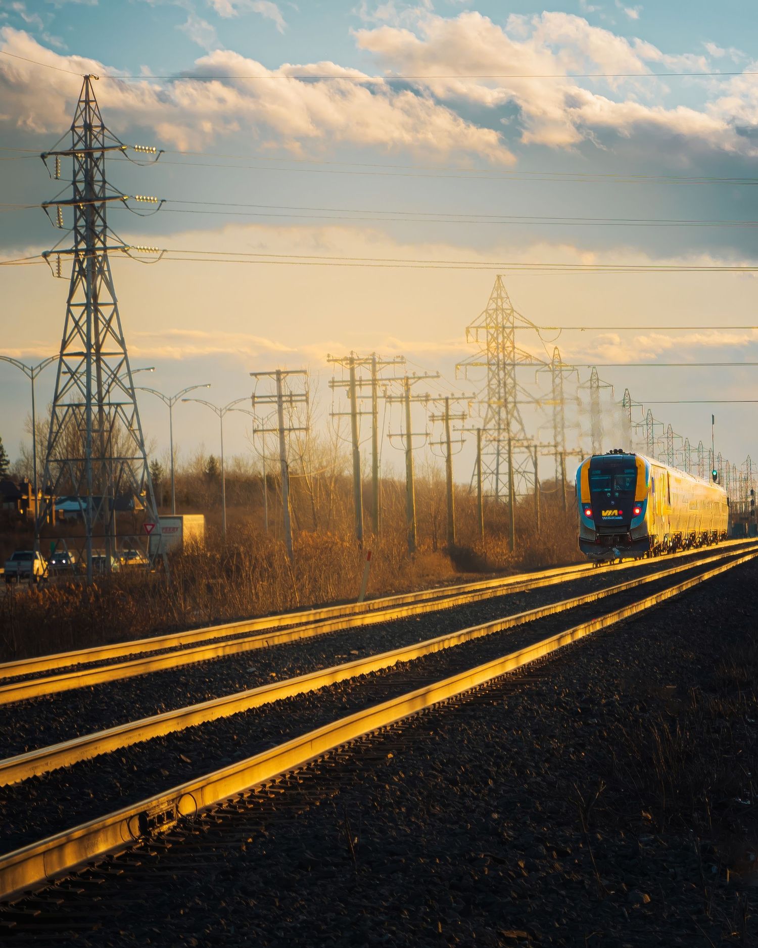Train tracks stretch into distance under golden sunset sky with power lines overhead.