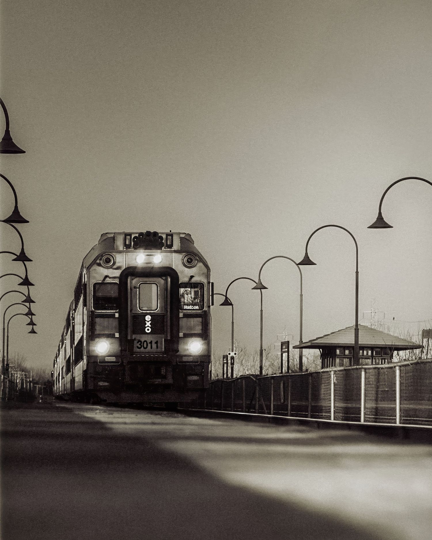 Vintage black and white train station platform with overhead lamps and railway tracks.