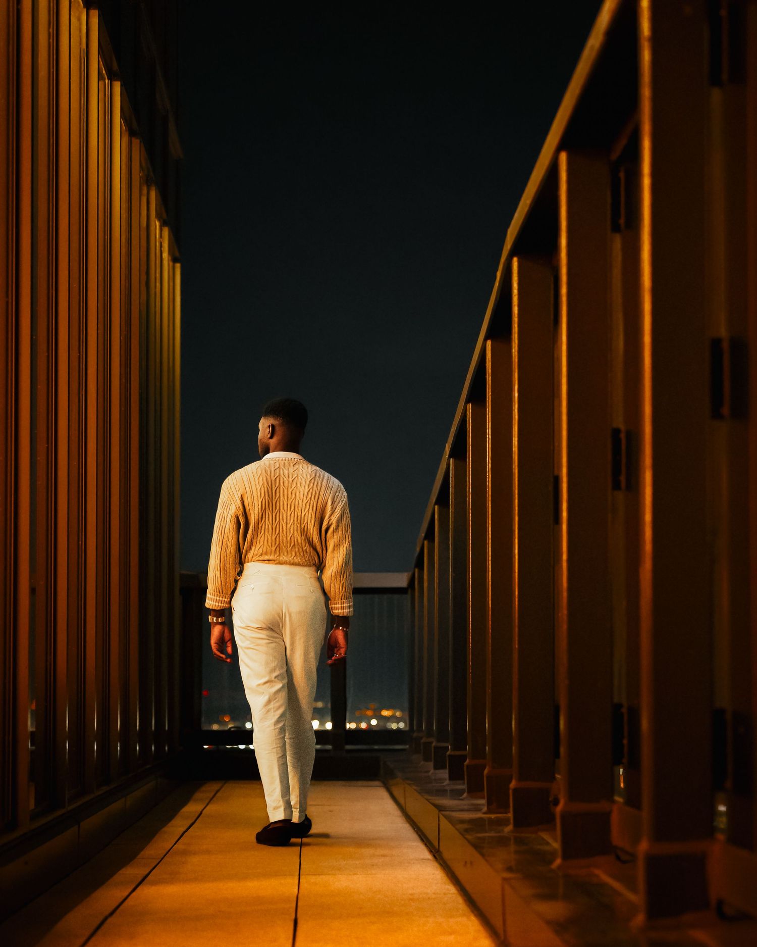 Artistic night photo of man walking along illuminated corridor in yellow lighting.