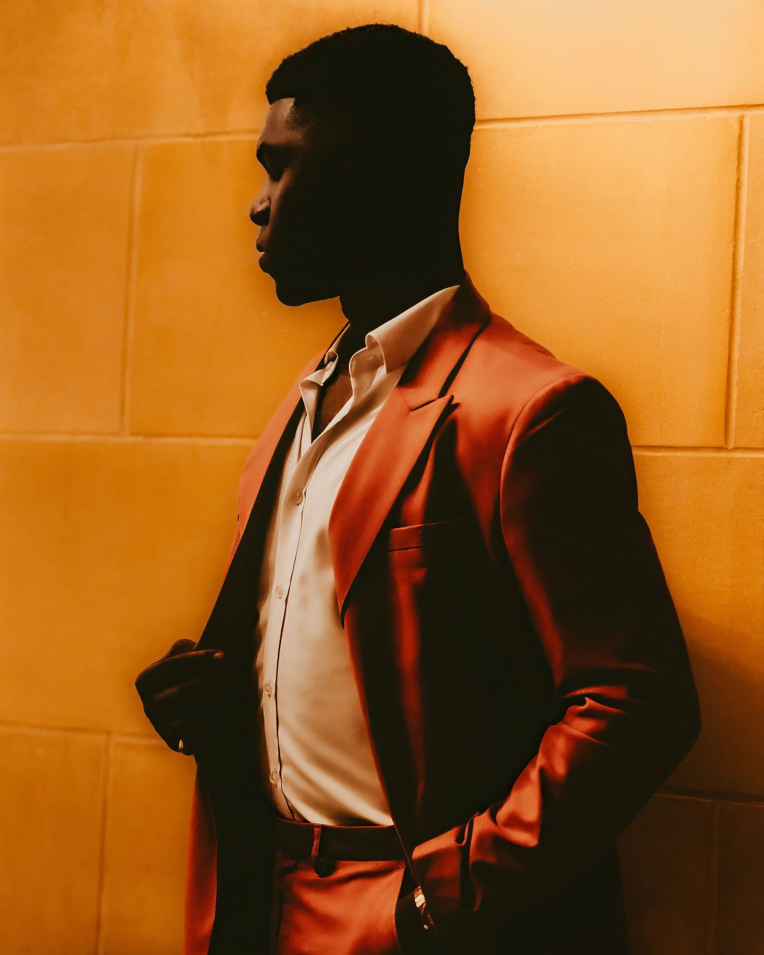 Side profile silhouette of man in orange blazer against warm-colored wall.