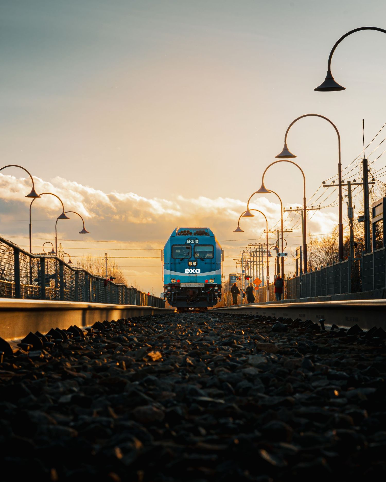 Sunset silhouette of street lamps and power lines along railway tracks.