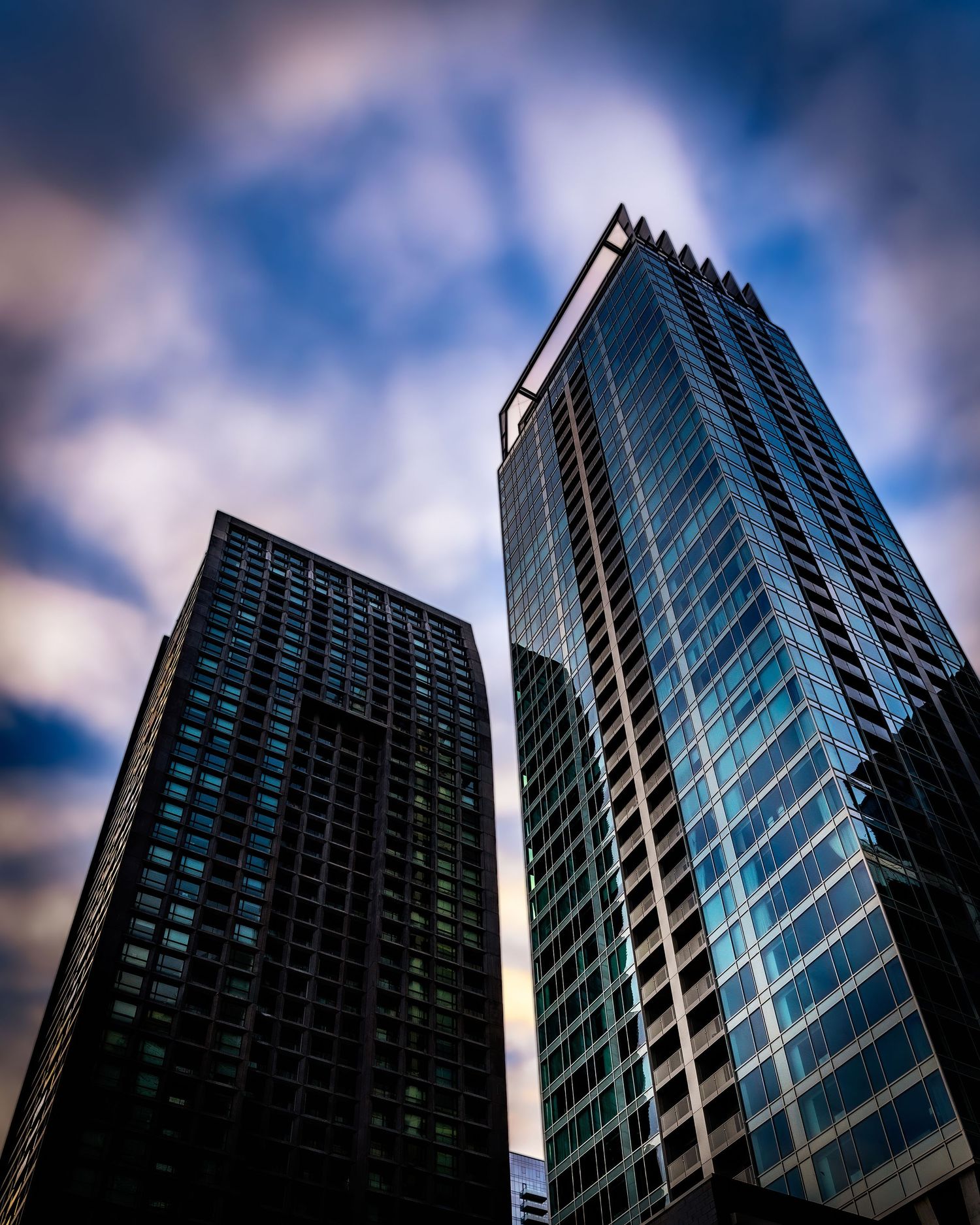 Modern glass skyscrapers shot from below against dramatic blue cloudy sky.
