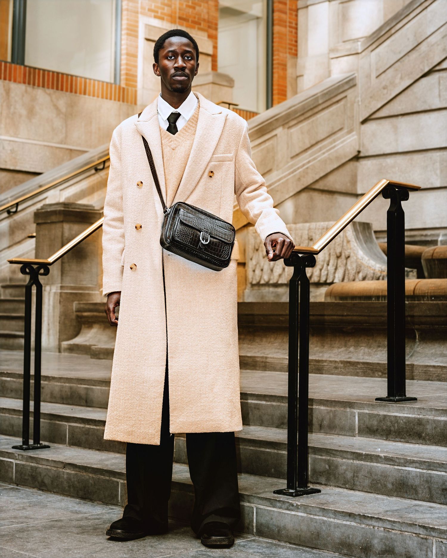 Stylish cream overcoat and black pants ensemble photographed against architectural backdrop.