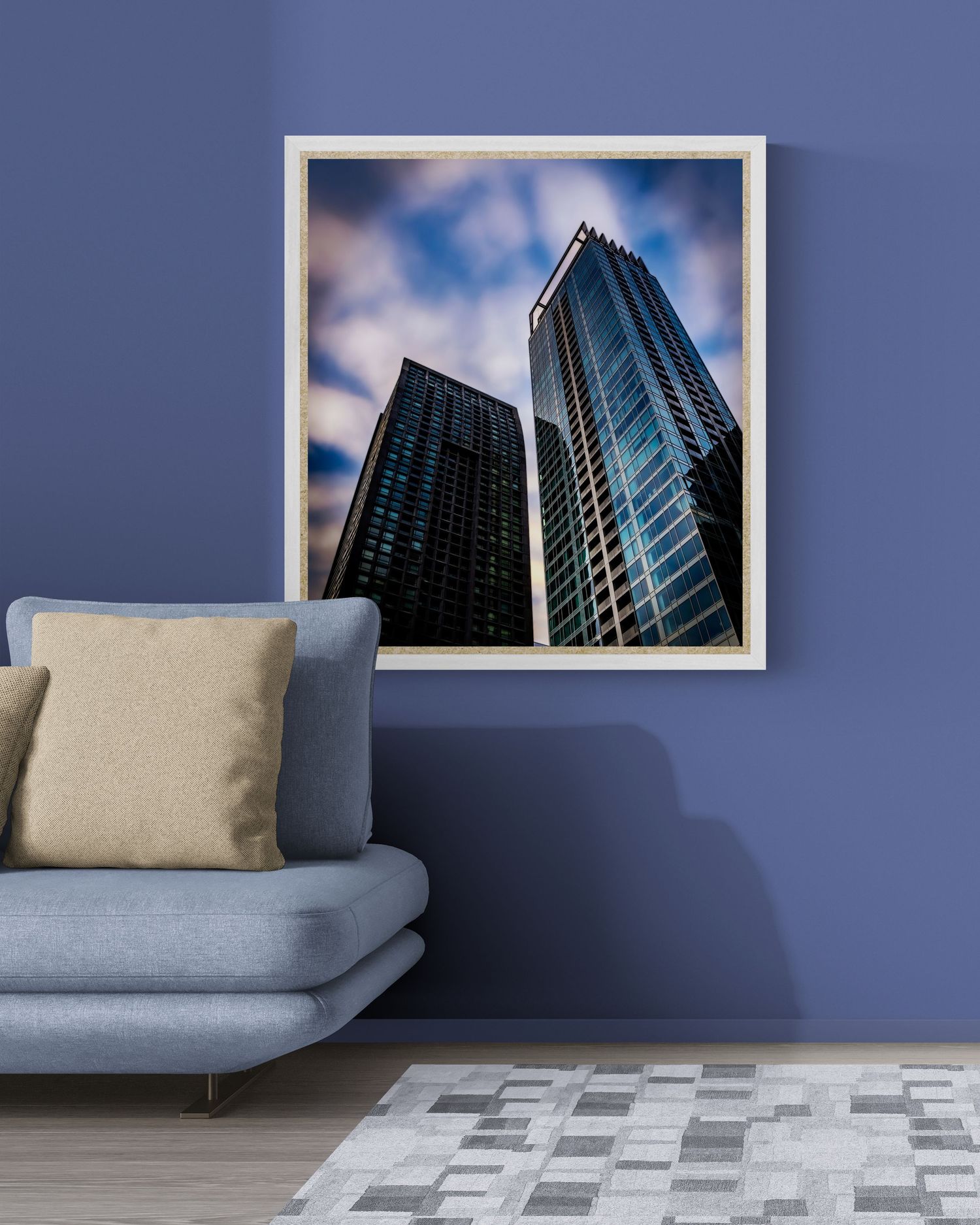 Framed photo of towering skyscrapers against a blue sky, displayed on a blue wall above a modern gray sofa.