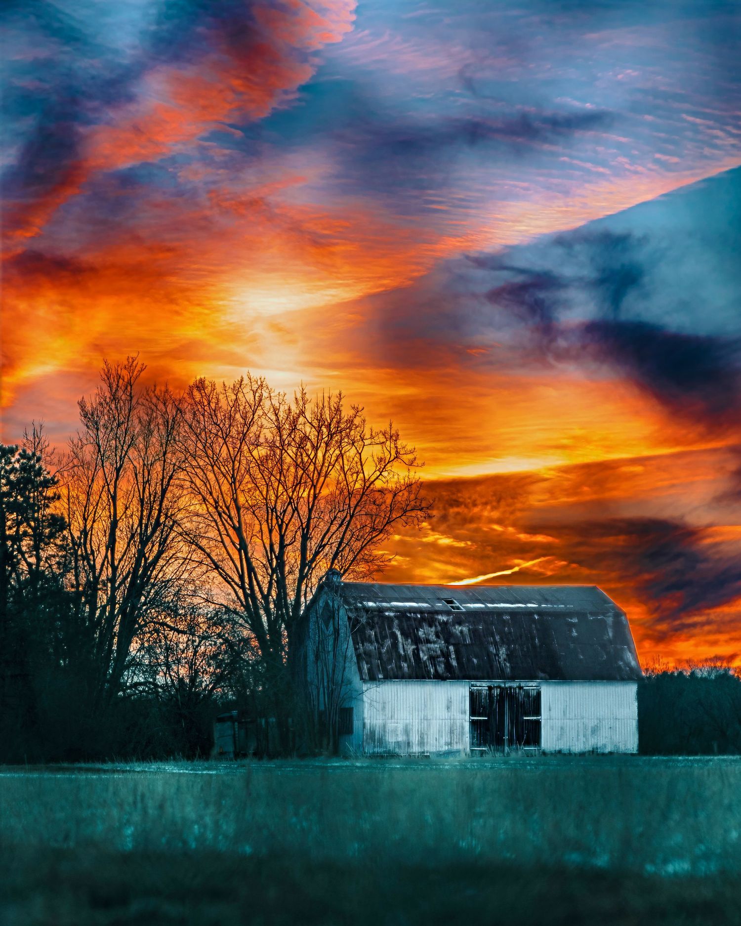 Dramatic sunset behind an old barn silhouette with fiery orange clouds and deep blue sky.