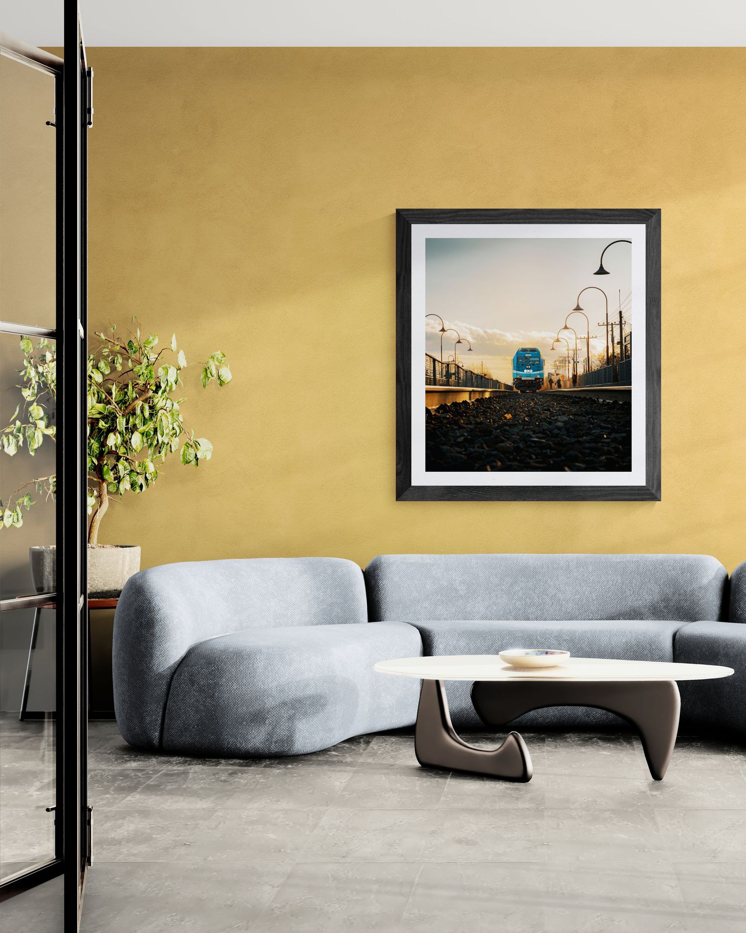 Modern living room with gray curved sofa, oval coffee table, and framed train photo on yellow wall.