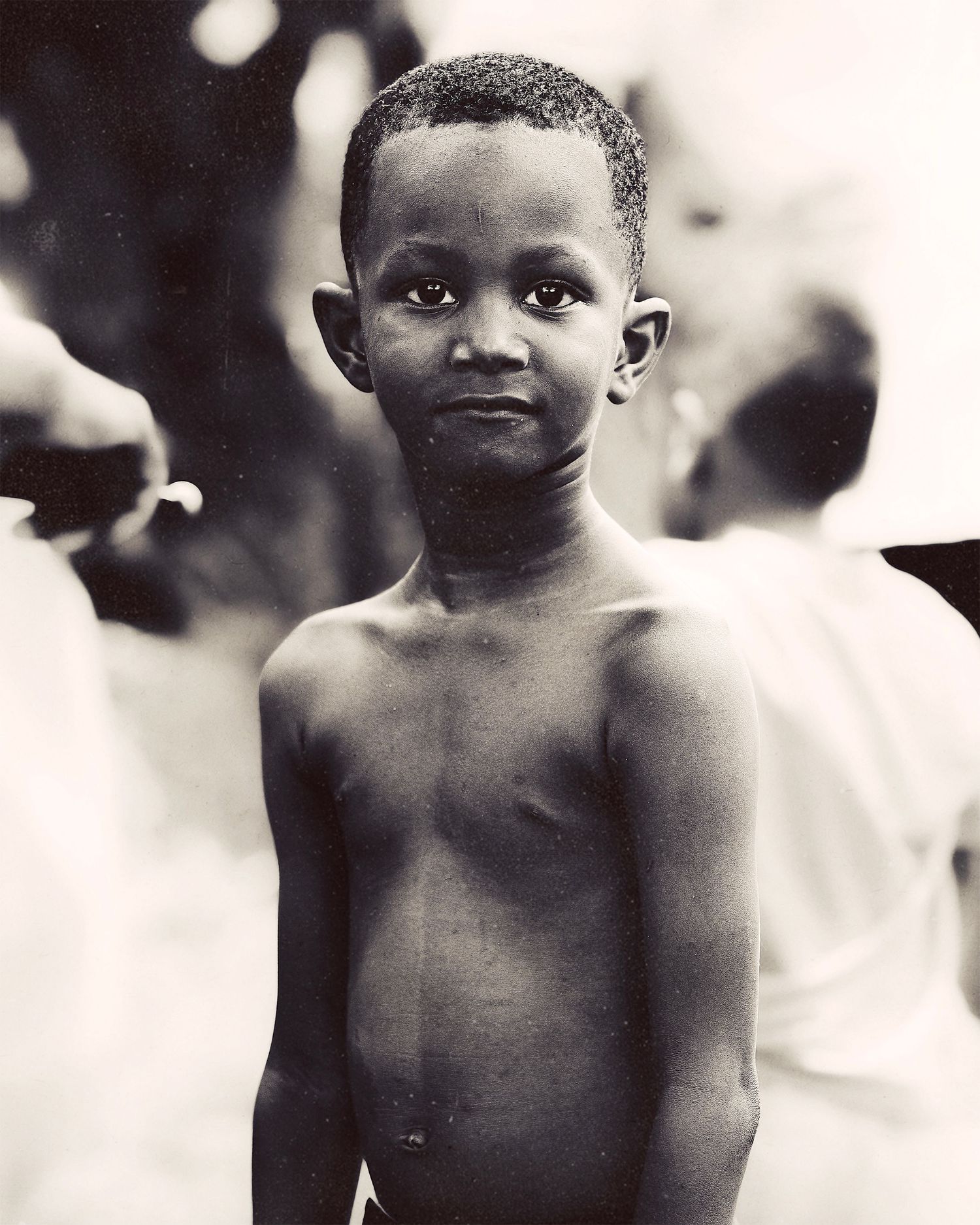 Black and white portrait photo of a young shirtless boy looking at the camera with a gentle expression.