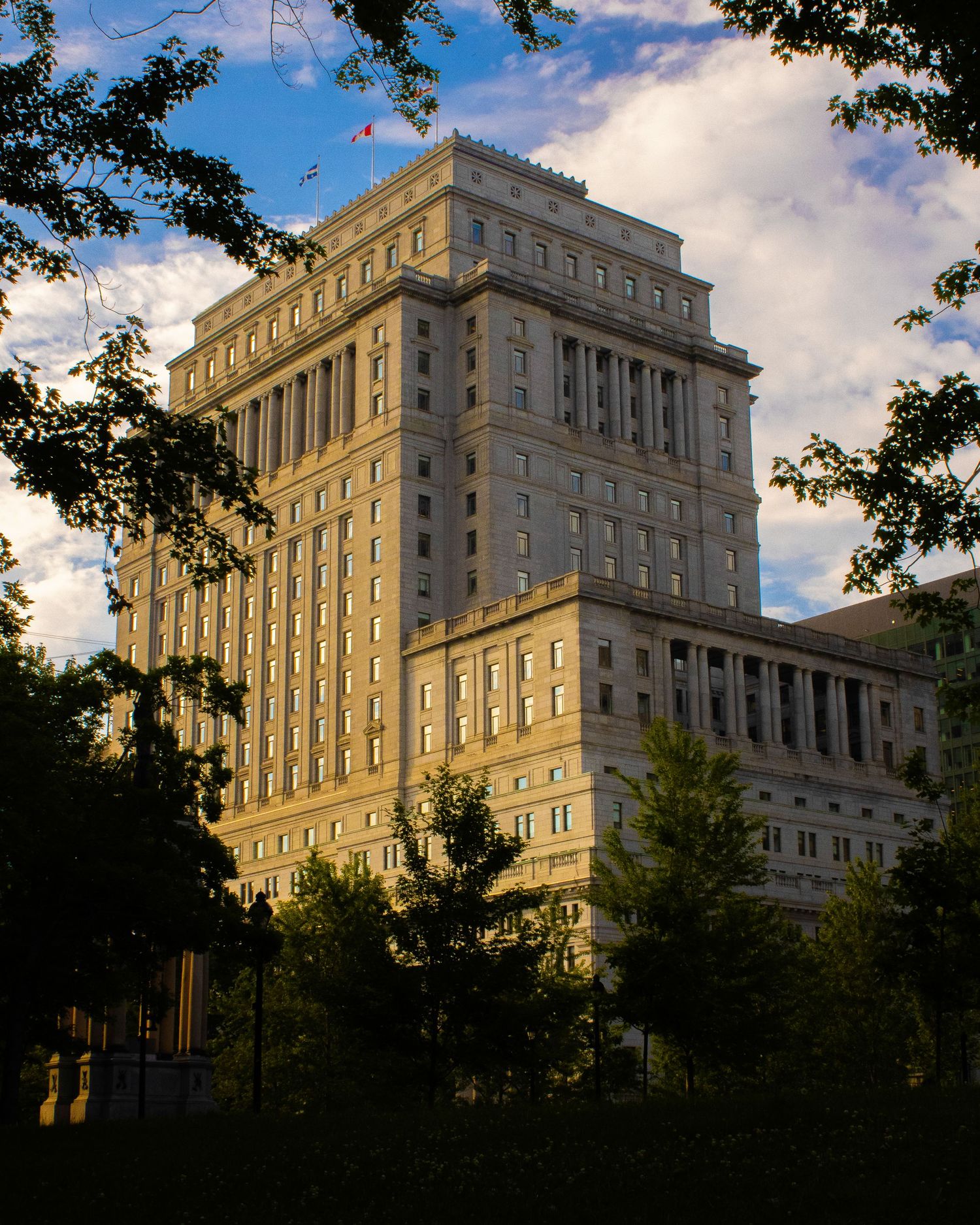 Historic stone government building photographed against blue sky with trees in foreground.