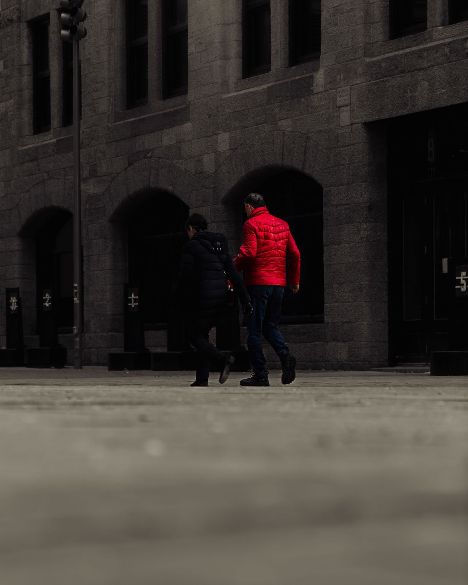 Urban scene with stone building facade and figures in red coats walking past.