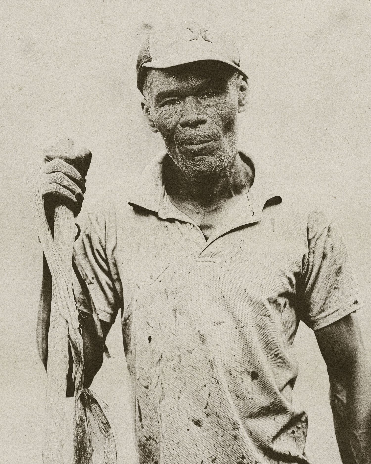 Vintage black and white photo of an elderly man in a cap and dirty shirt, holding a wooden tool or stick.