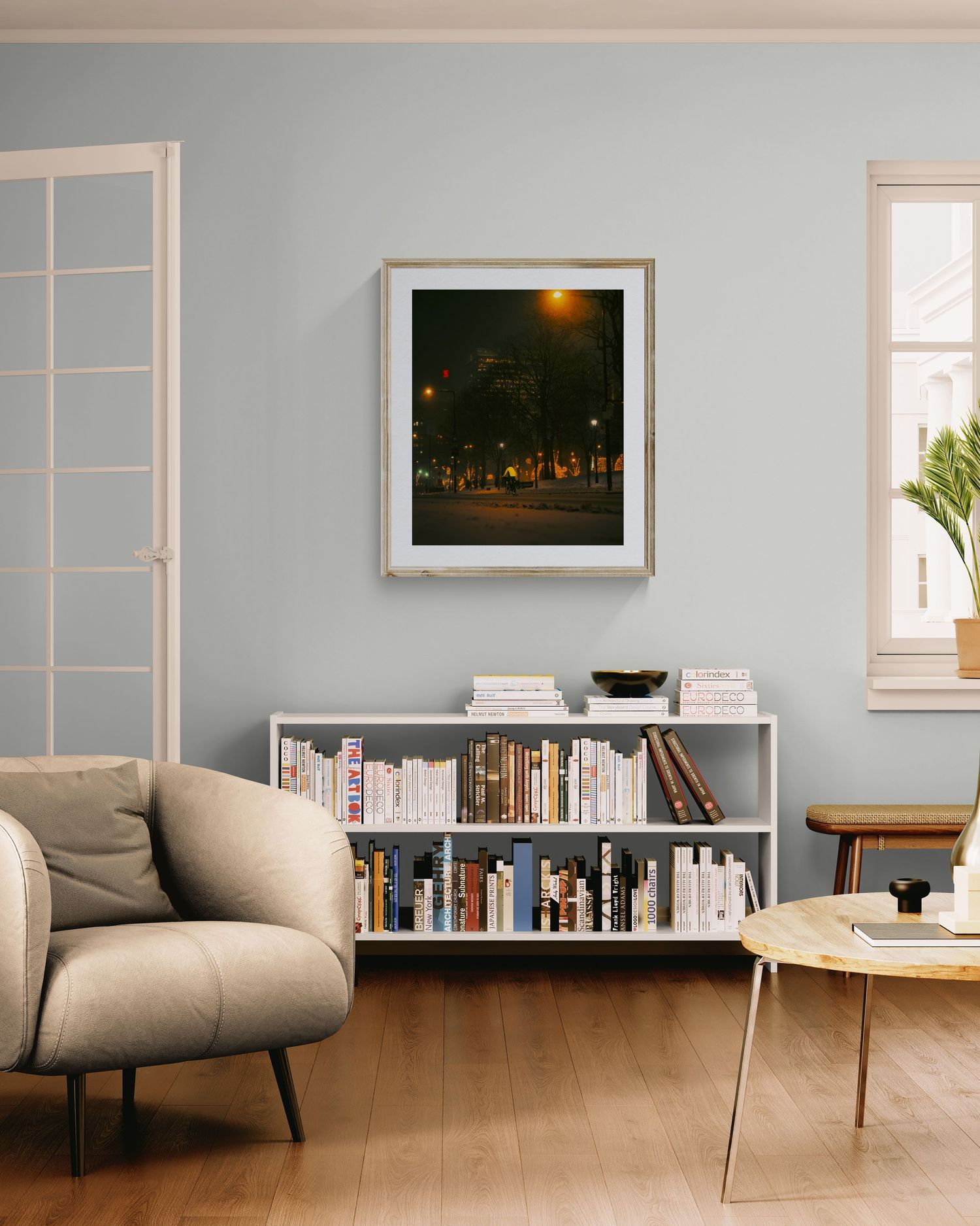 Modern living room with bookshelf, armchair, and framed night street photo art on light blue wall.