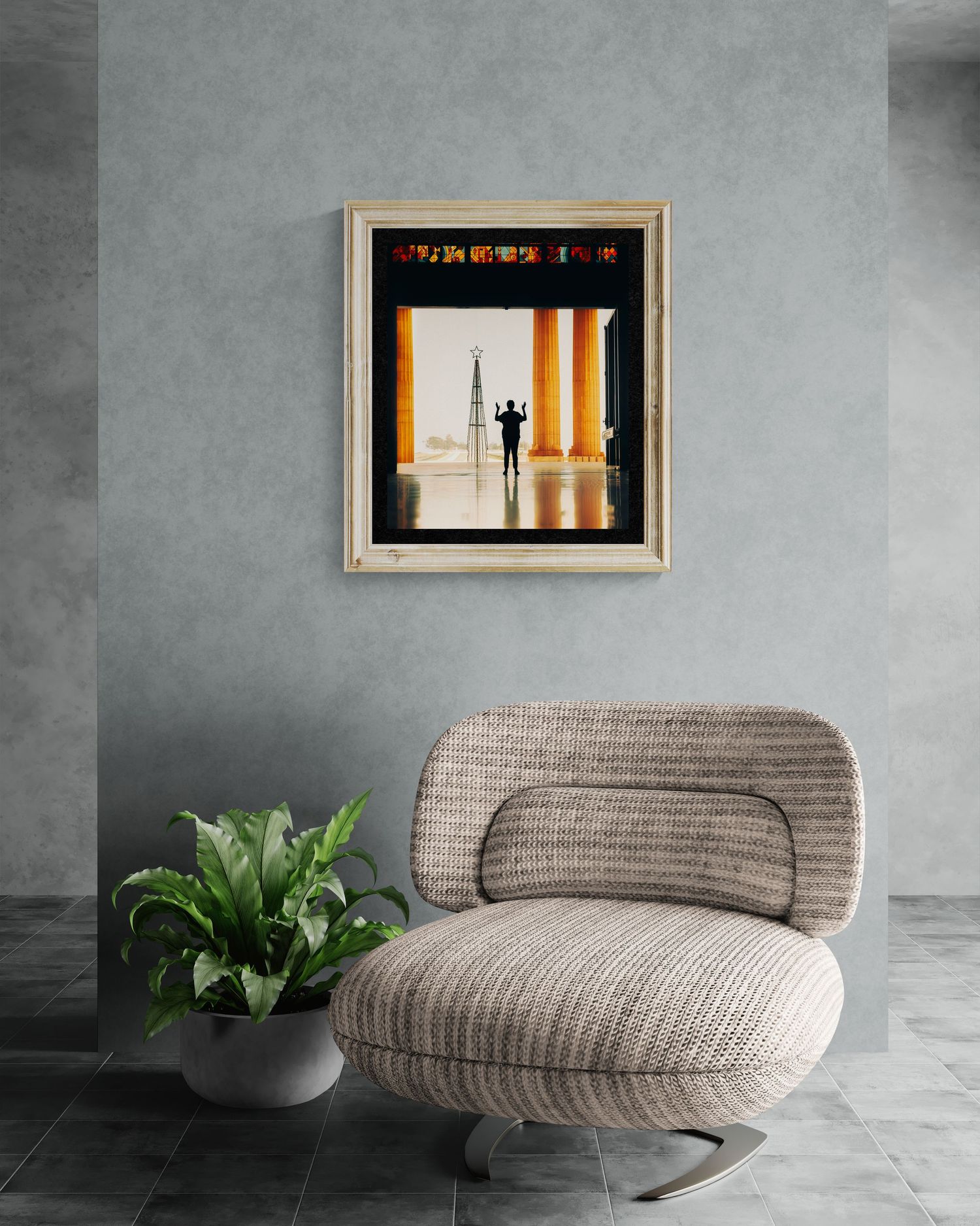 Framed artwork of a silhouette between columns hangs on a gray wall above a beige curved chair and green plant.