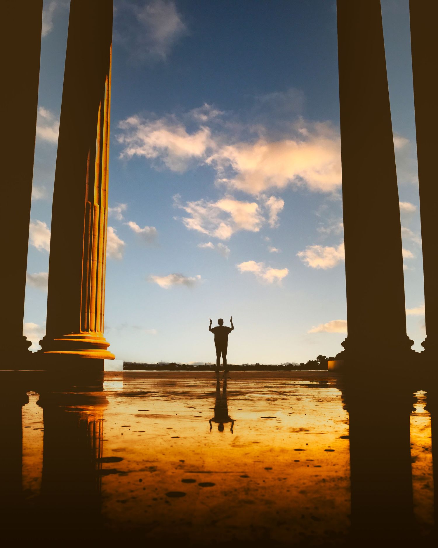 Silhouetted columns frame a dramatic sunset landscape with a lone figure standing on the horizon against an orange sky.