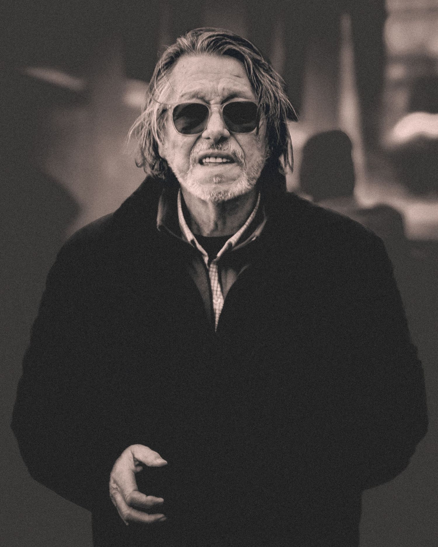 Person in black winter coat and sunglasses photographed in moody black and white style.