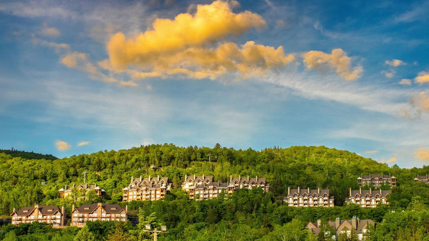 Golden sunset clouds roll over green mountains with luxury condominiums nestled in the forest.