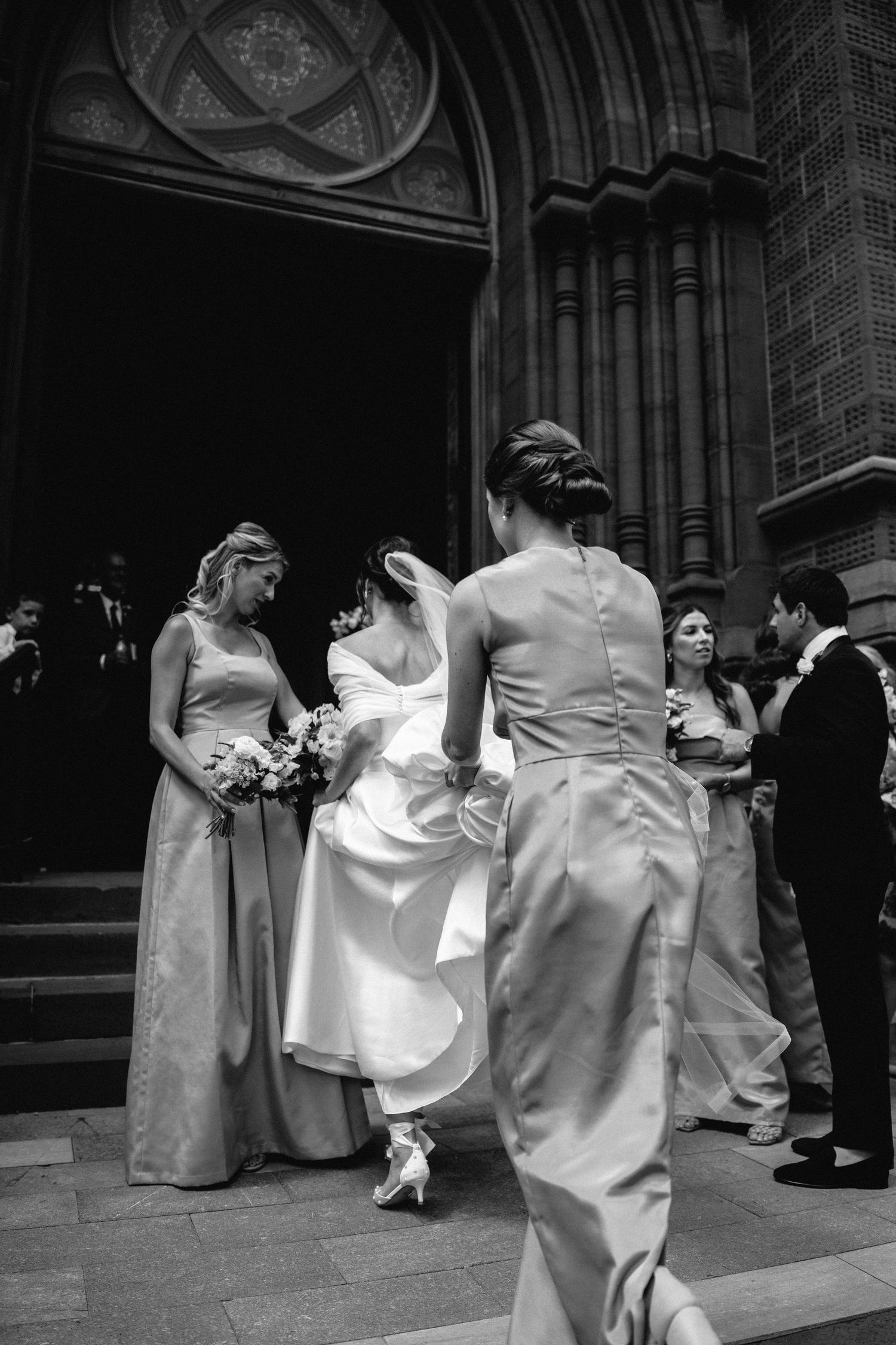A Bridesmaid helping the bride by holding the wedding veil while walking up the stairs of St John The Baptist Cathedral's church, Charleston