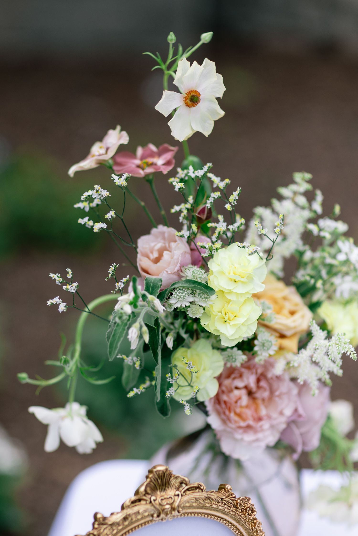 Delicate wedding centerpiece with pastel roses, lisianthus, and wildflowers in shades of blush, yellow, and ivory, arranged in a soft garden