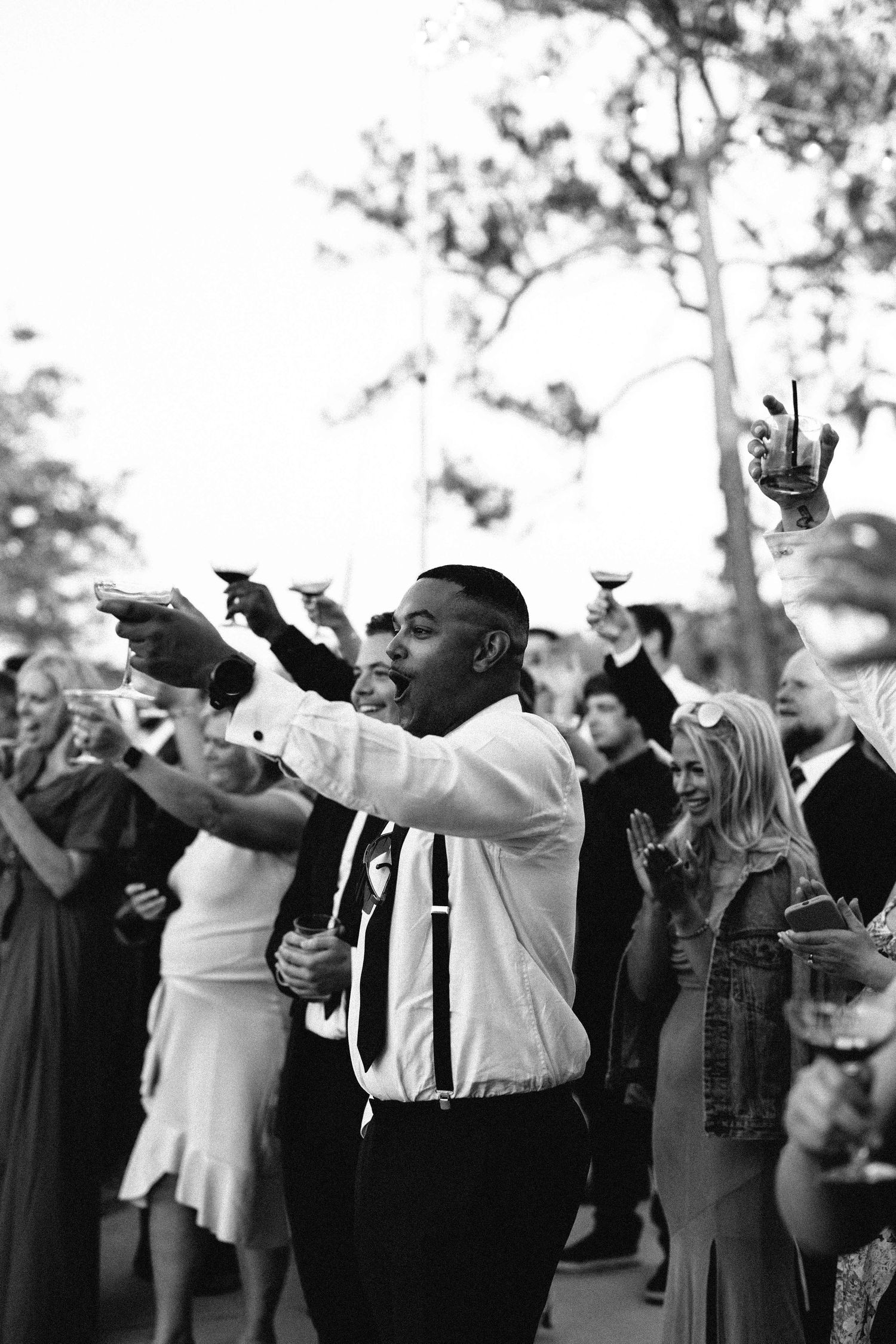 a black and white image of wedding guests toasting their drinks to the bride and groom