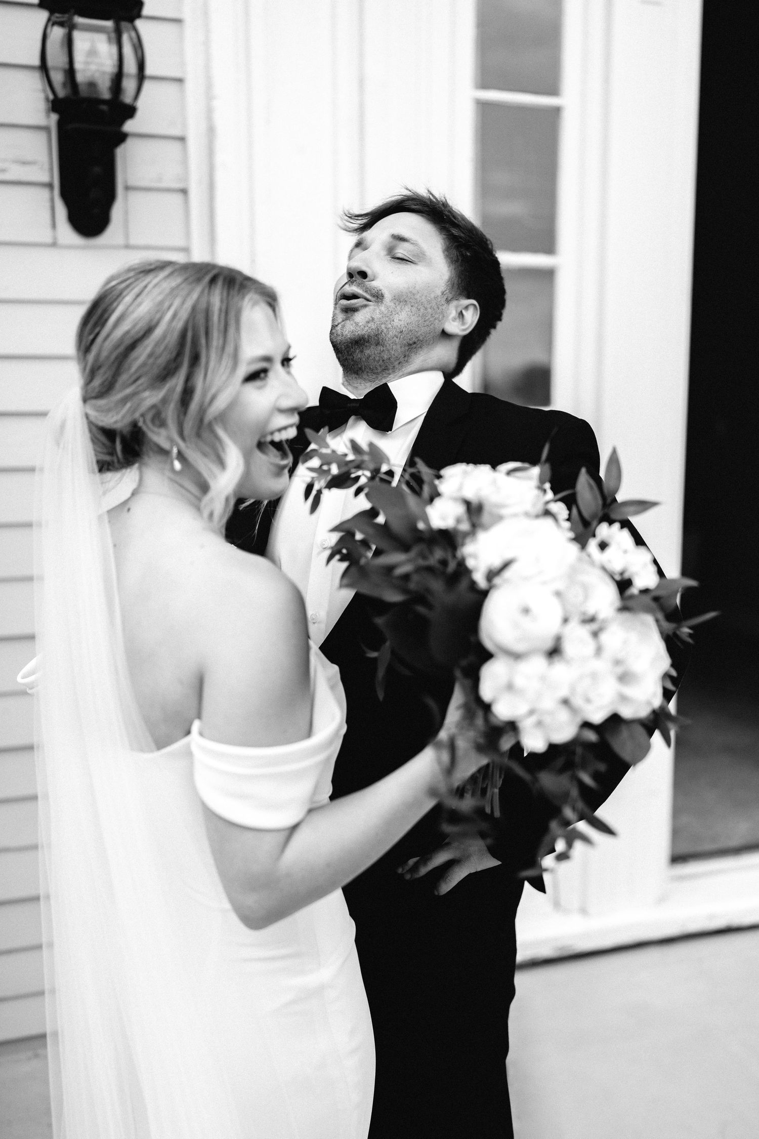 a black and white image of a bride laughing while the groom expresses his excitement by looking up into the air