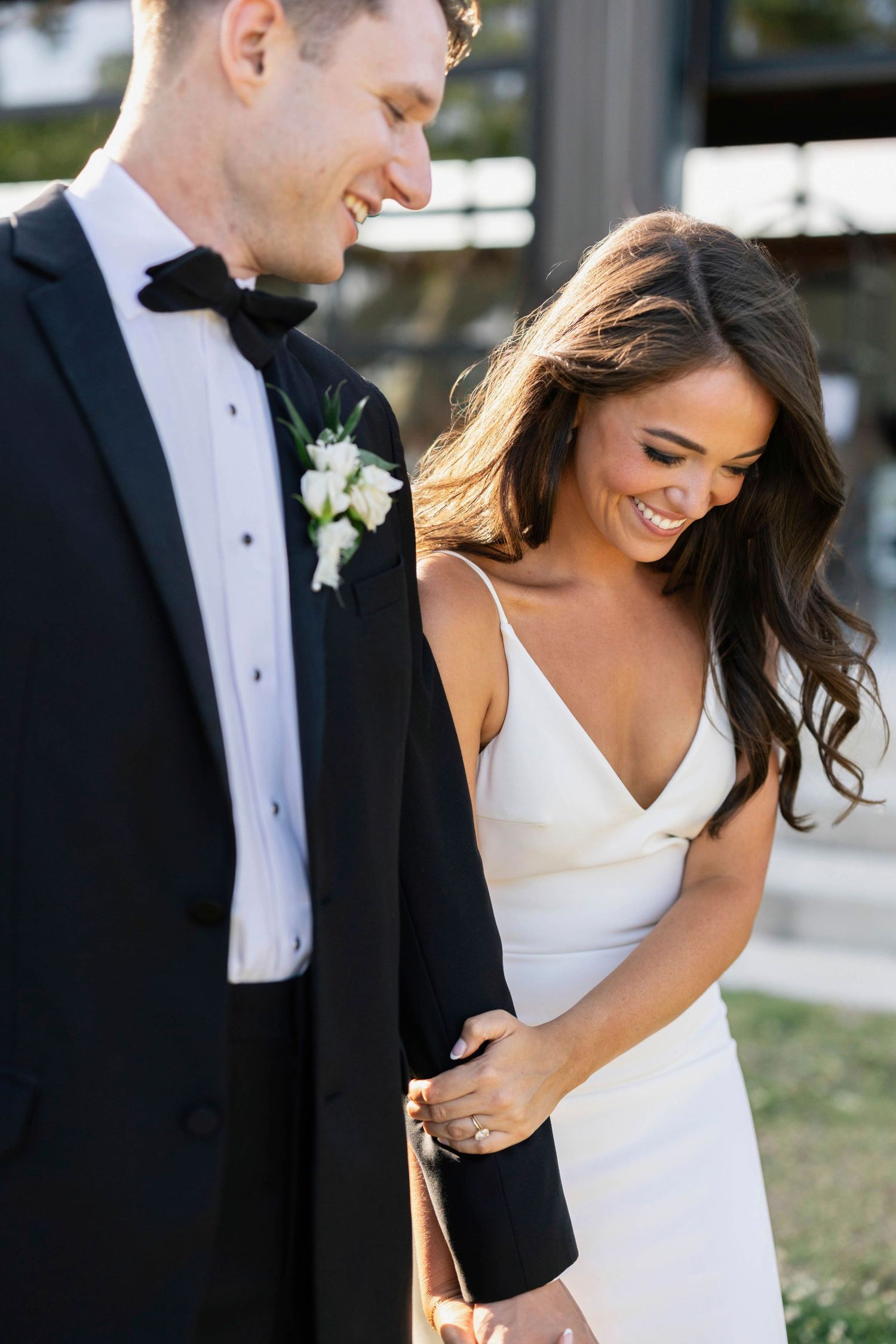 A bride walking while holding onto her grooms arm while they both smile candidly.