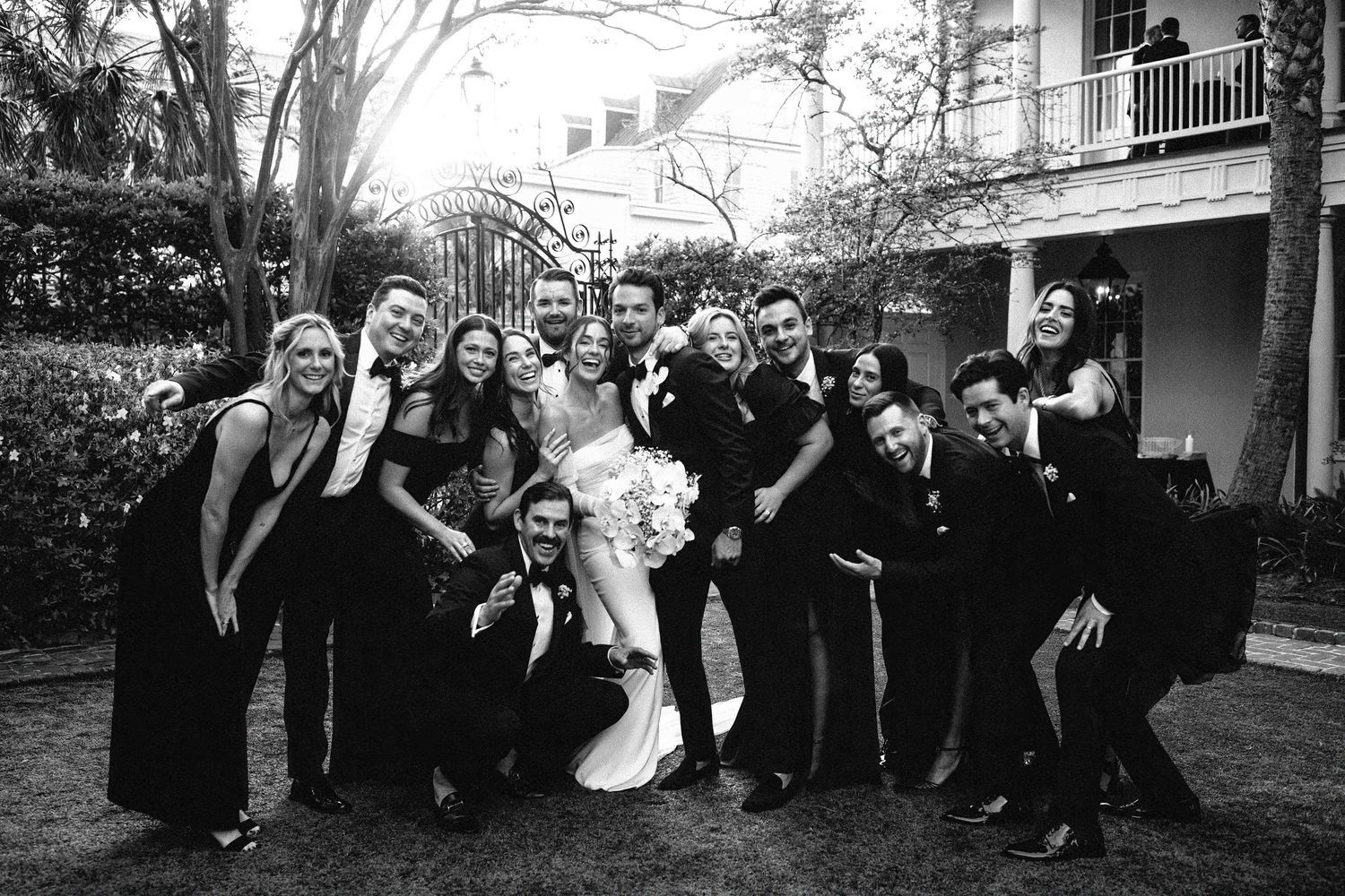 A large wedding party celebrating the bride and groom with cheers and laughter in the courtyard of the William Aiken House, Charleston.