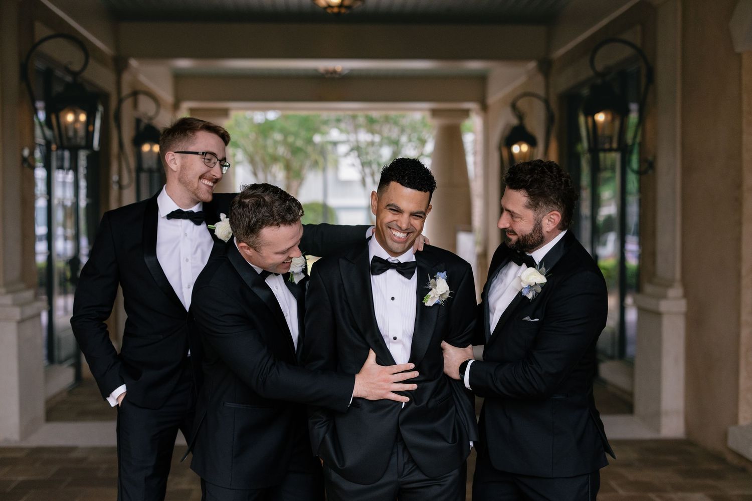 Three formally dressed groomsmen wearing tuxedos, hyping up the happy groom