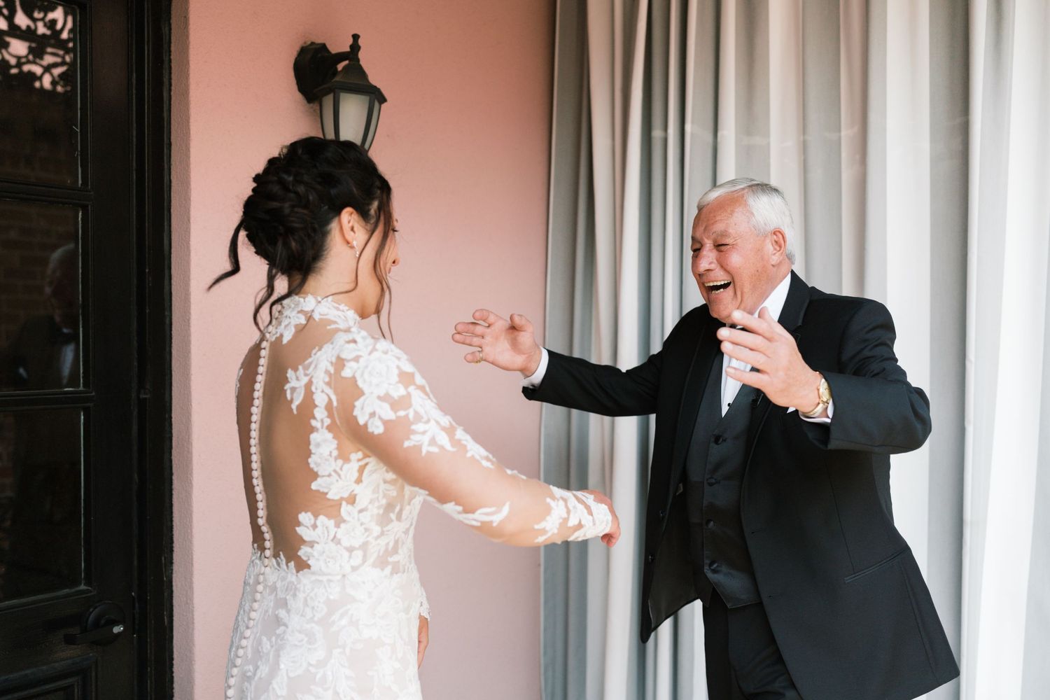 Father joyfully reaching out to embrace his daughter in a lace wedding gown during their first look.