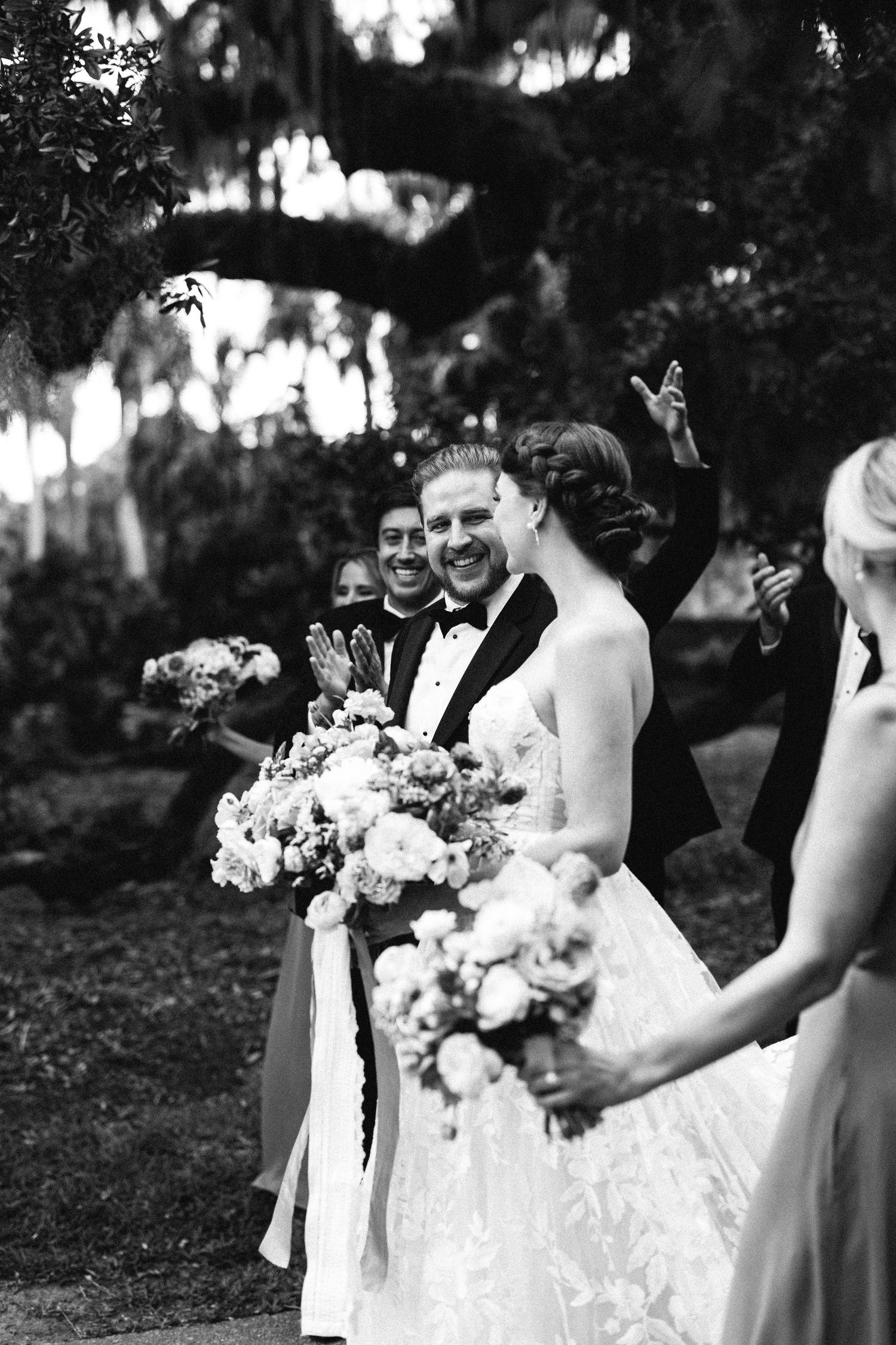 a black and white image of a bridal party walking together while the groom smiles towards his bride.