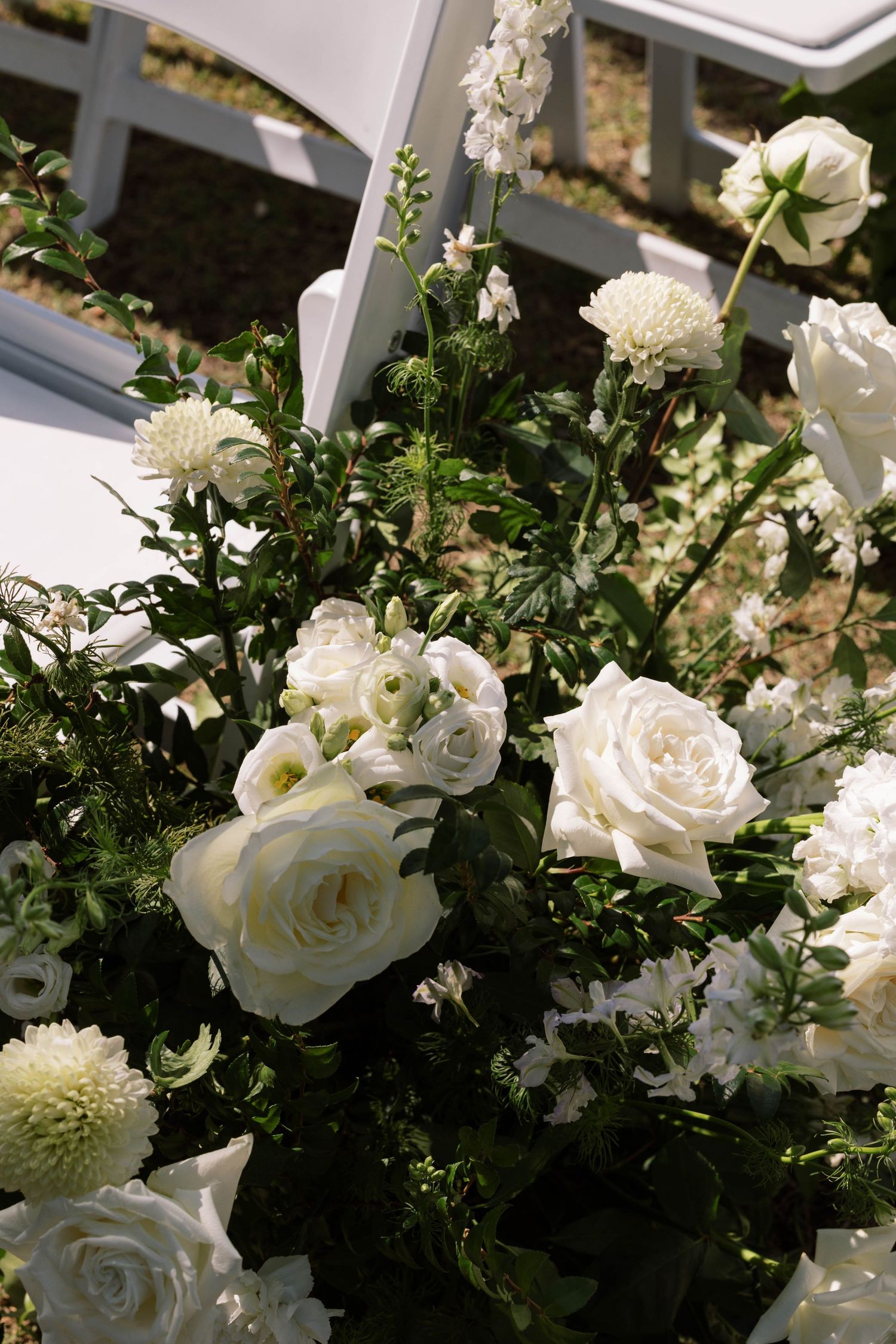 A wedding floral aisle arrangement with white garden roses, dahlisa, ranunculus flowers and greenery