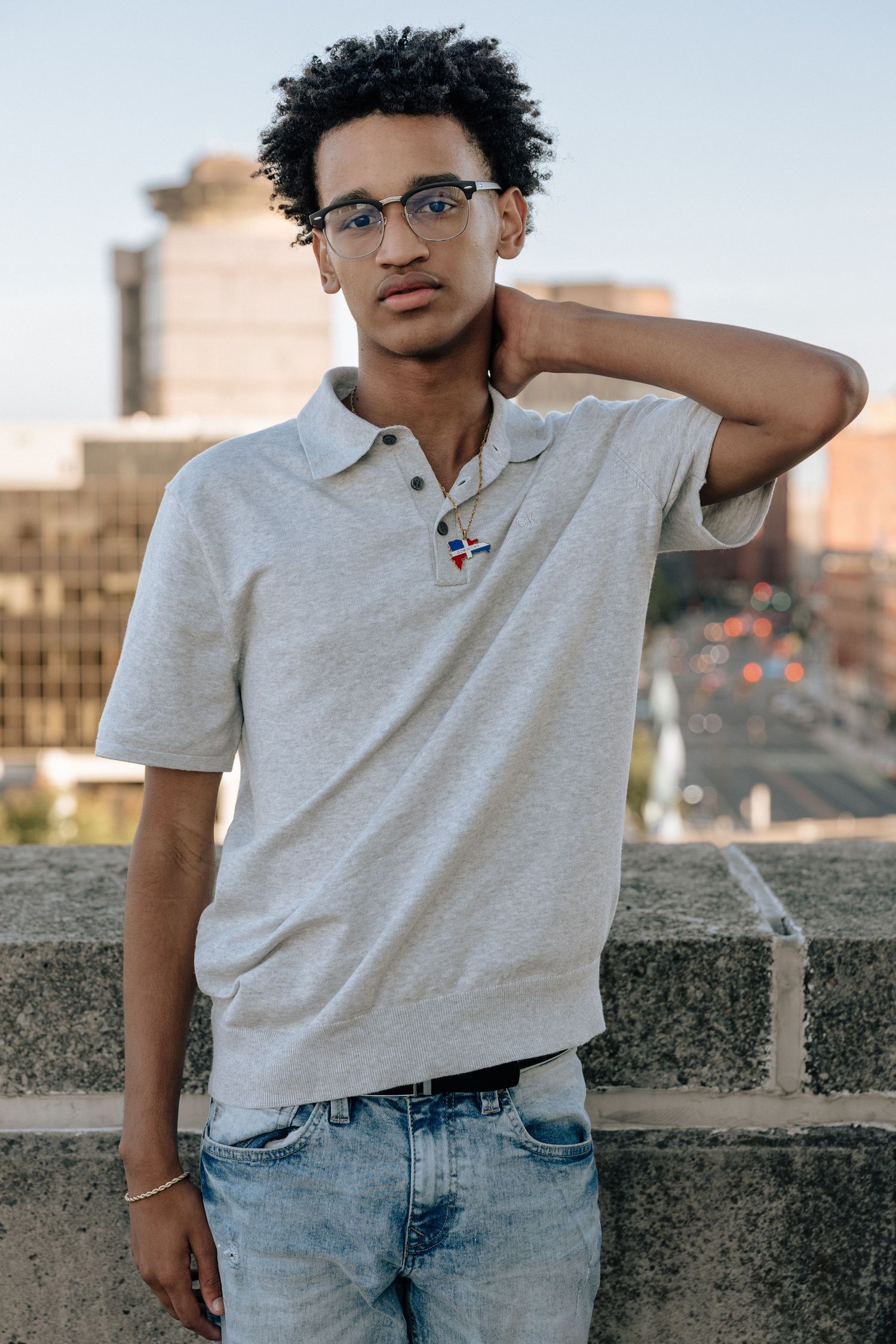 Person in casual gray t-shirt and jeans poses against stone wall during sunset lighting.