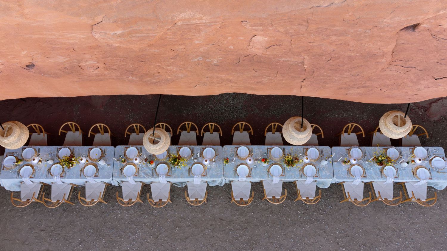Aerial view of an elegant outdoor dining table set for a large group against a red rock canyon wall.